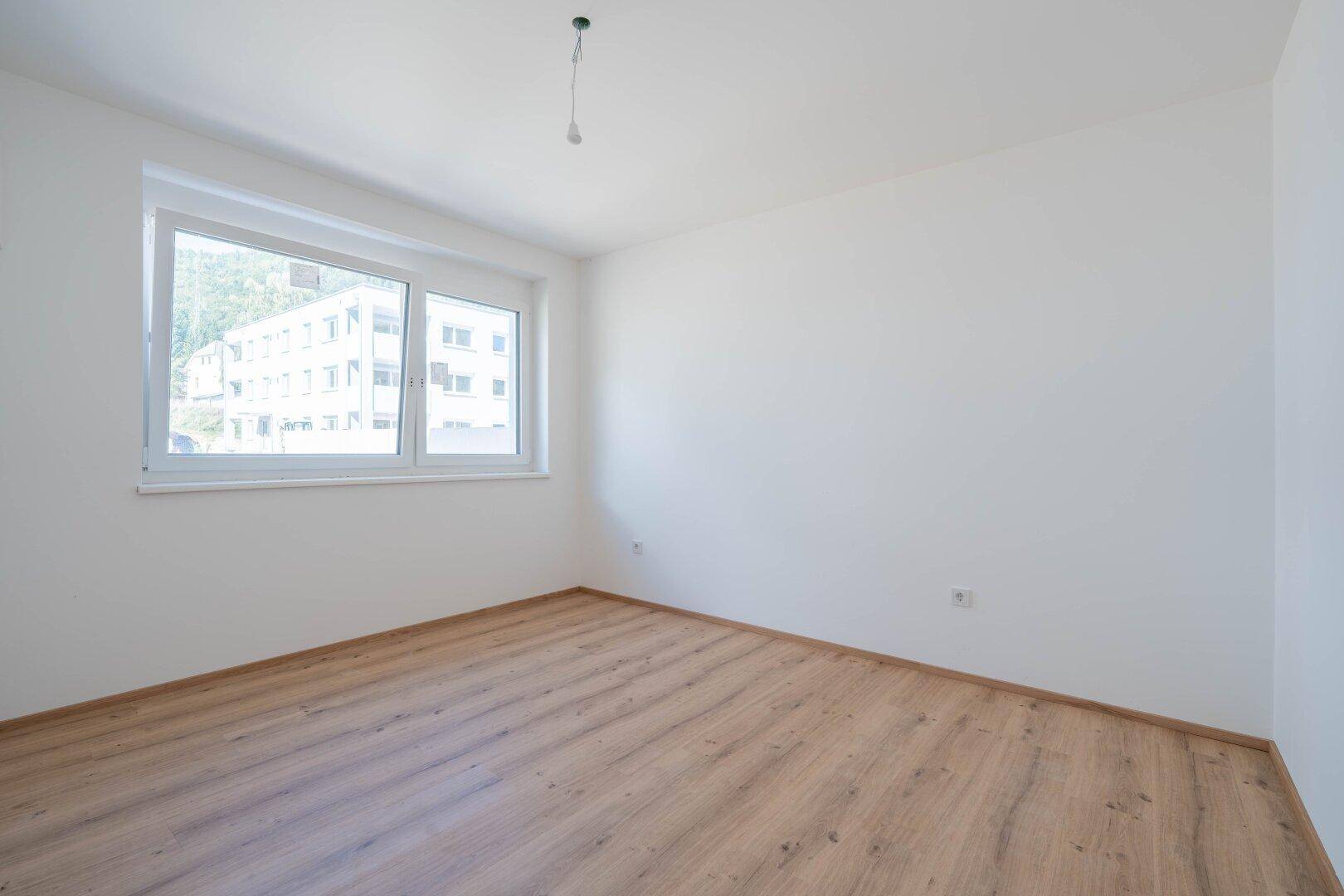 Helles Schlafzimmer mit Laminatboden und großem Fenster, bereit für die Einrichtung.
