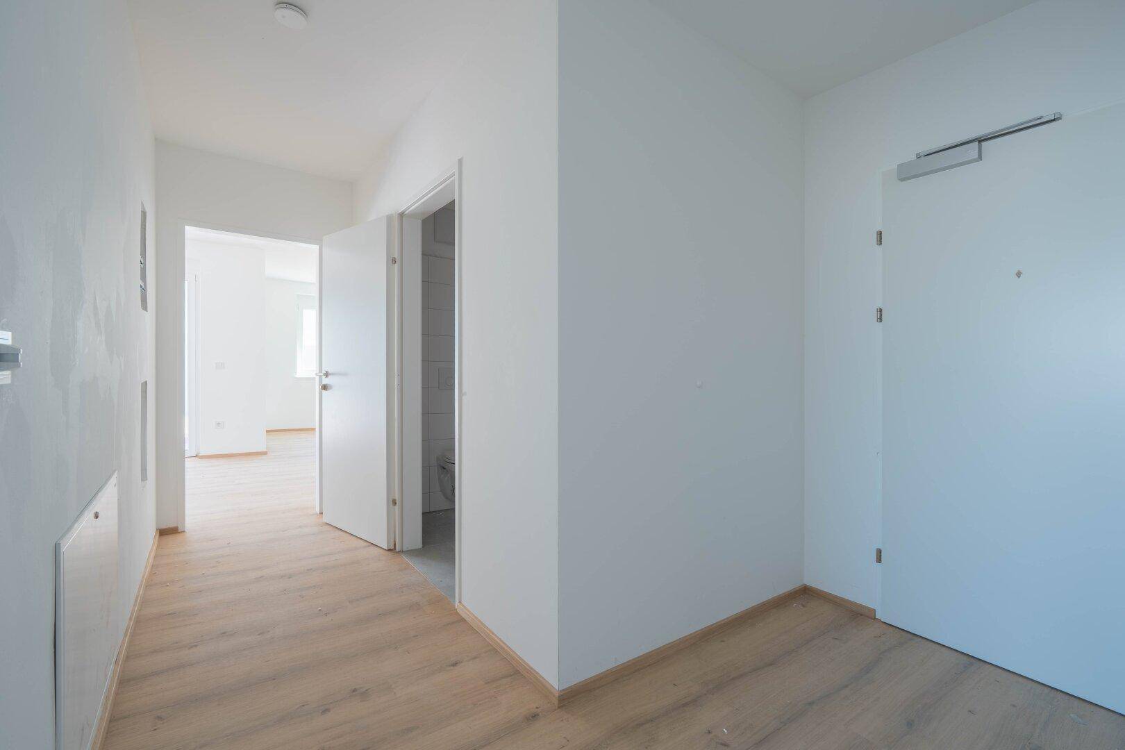 Heller Flur mit Laminatboden und weißen Wänden, der zu verschiedenen Räumen führt.