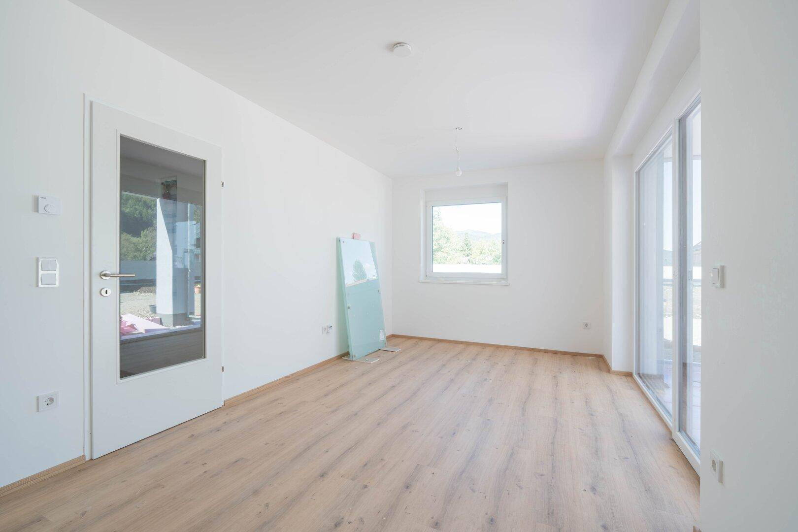 Heller, leerer Raum mit Laminatboden, weißen Wänden und Zugang zu einem Außenbereich.
