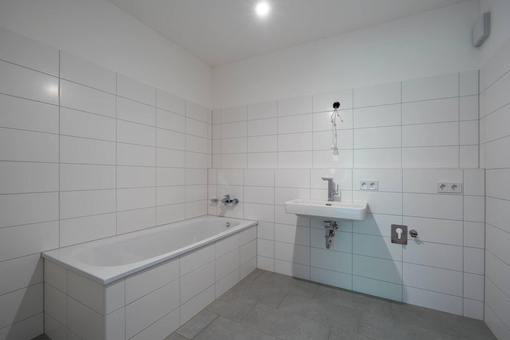 Modernes Badezimmer mit weißen Fliesen, Badewanne und Waschbecken, in neuwertigem Zustand.
