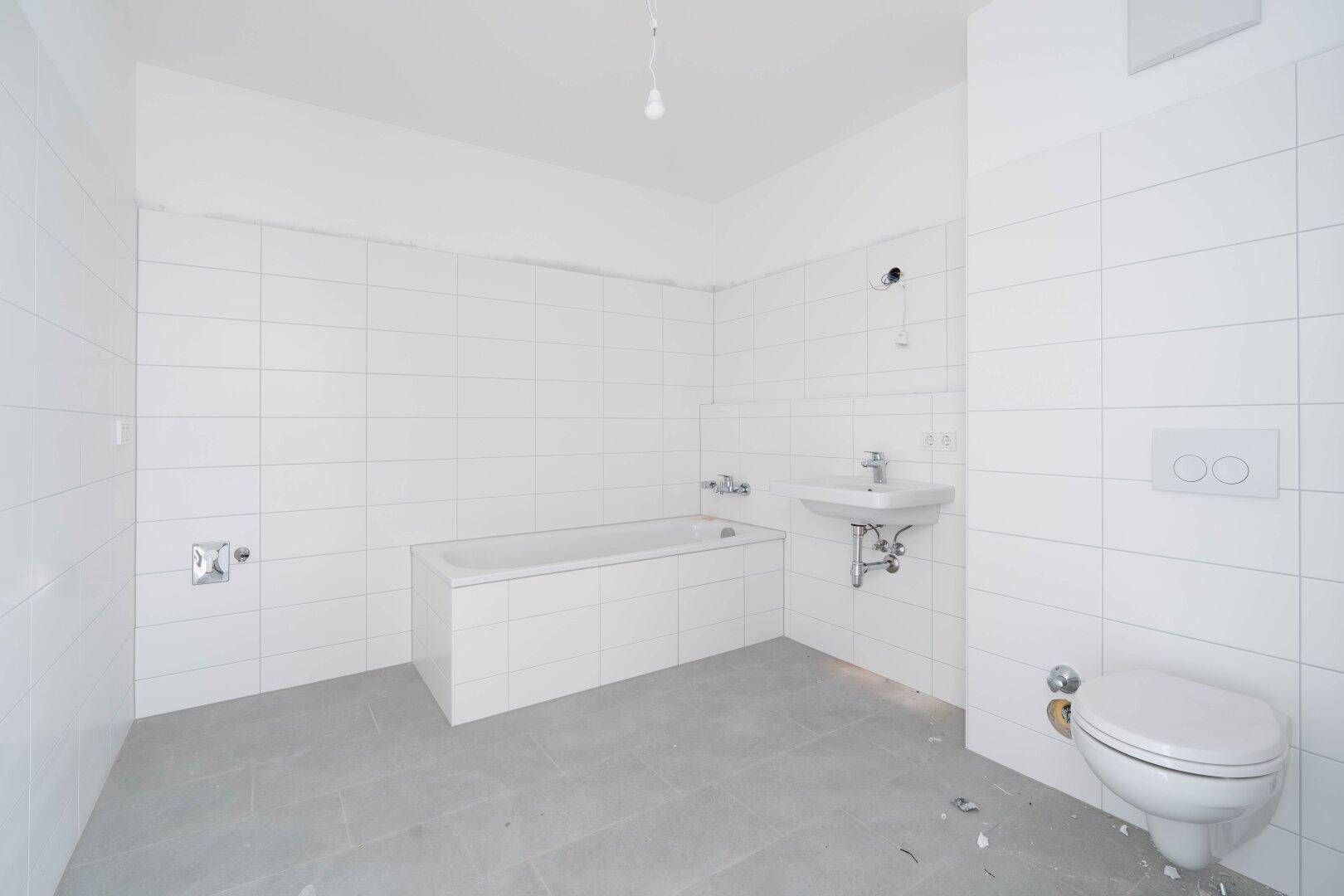 Modernes Badezimmer mit weißen Wandfliesen, grauen Bodenfliesen, Badewanne und wandhängendem WC.