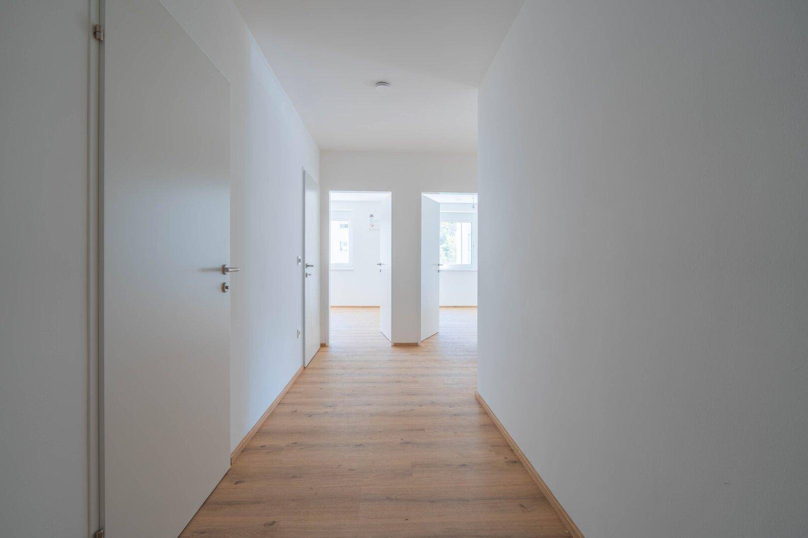 Heller Flur mit Laminatboden und mehreren weißen Türen, die zu den angrenzenden Räumen führen.