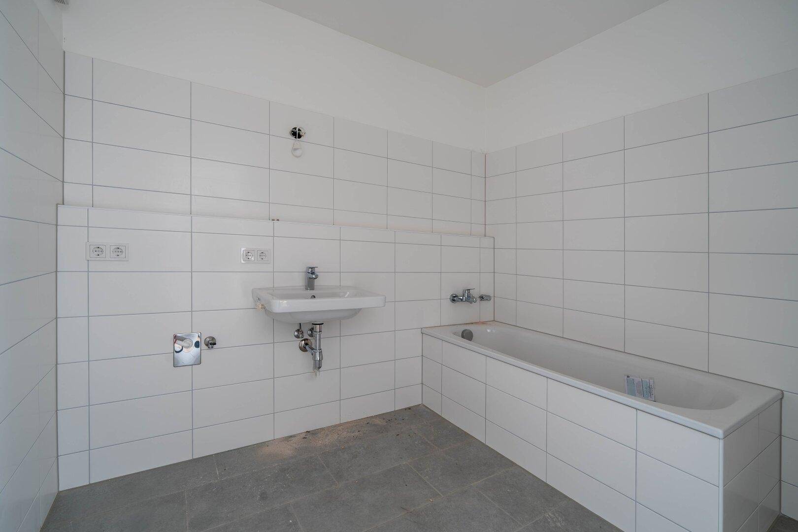 Unfertiges Badezimmer mit weißen Wandfliesen, Badewanne und Waschbecken, bereit für den Ausbau.