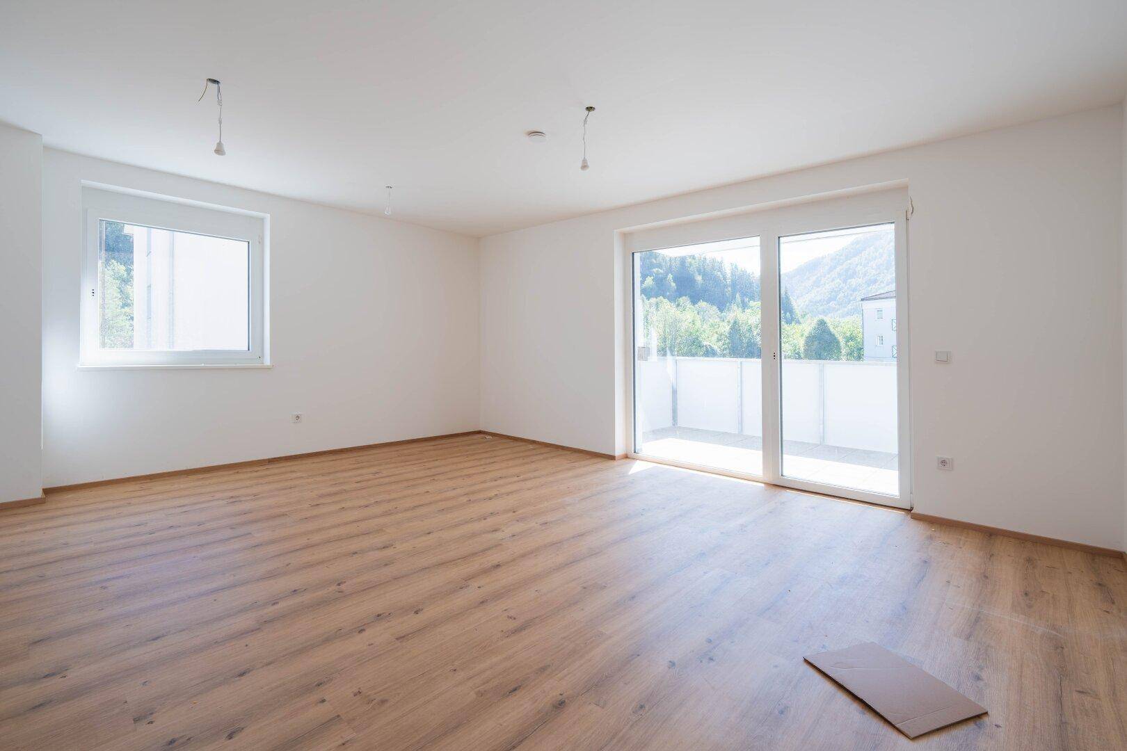 Helles Wohnzimmer mit Laminatboden, großen Fenstern und Zugang zu einem Balkon mit Bergblick.