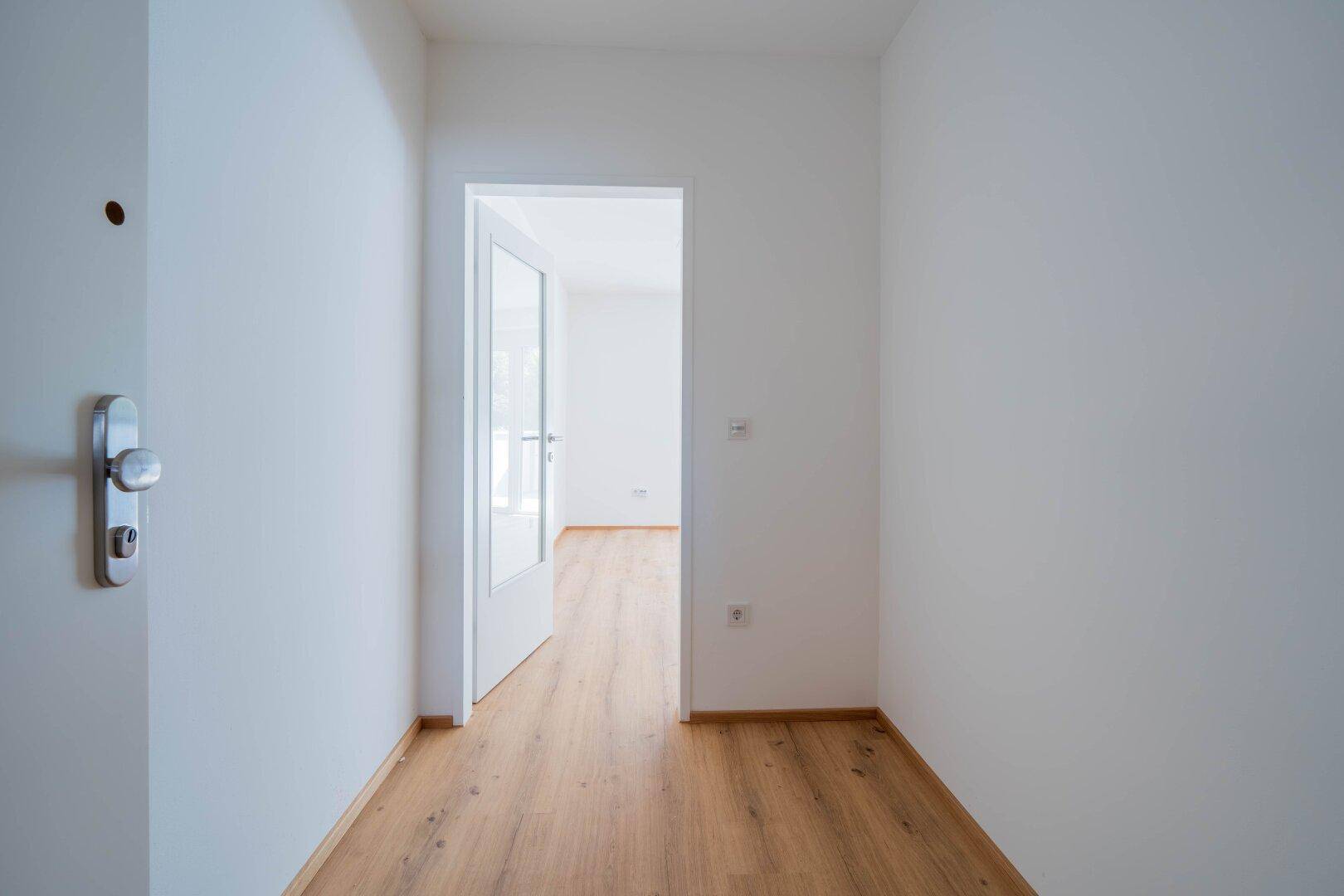 Heller Flur mit Laminatboden und weiß gestrichenen Wänden, der zu weiteren Räumen führt.