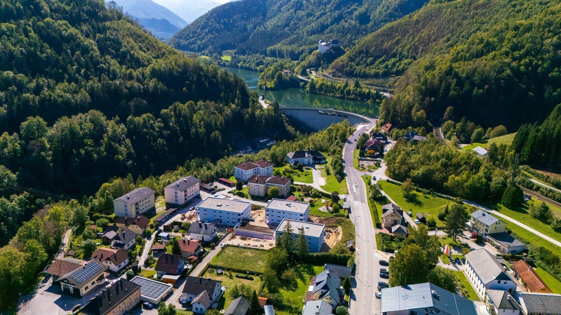 Luftaufnahme eines Dorfes in einem grünen Tal mit Fluss, Bergen und Wohngebäuden.
