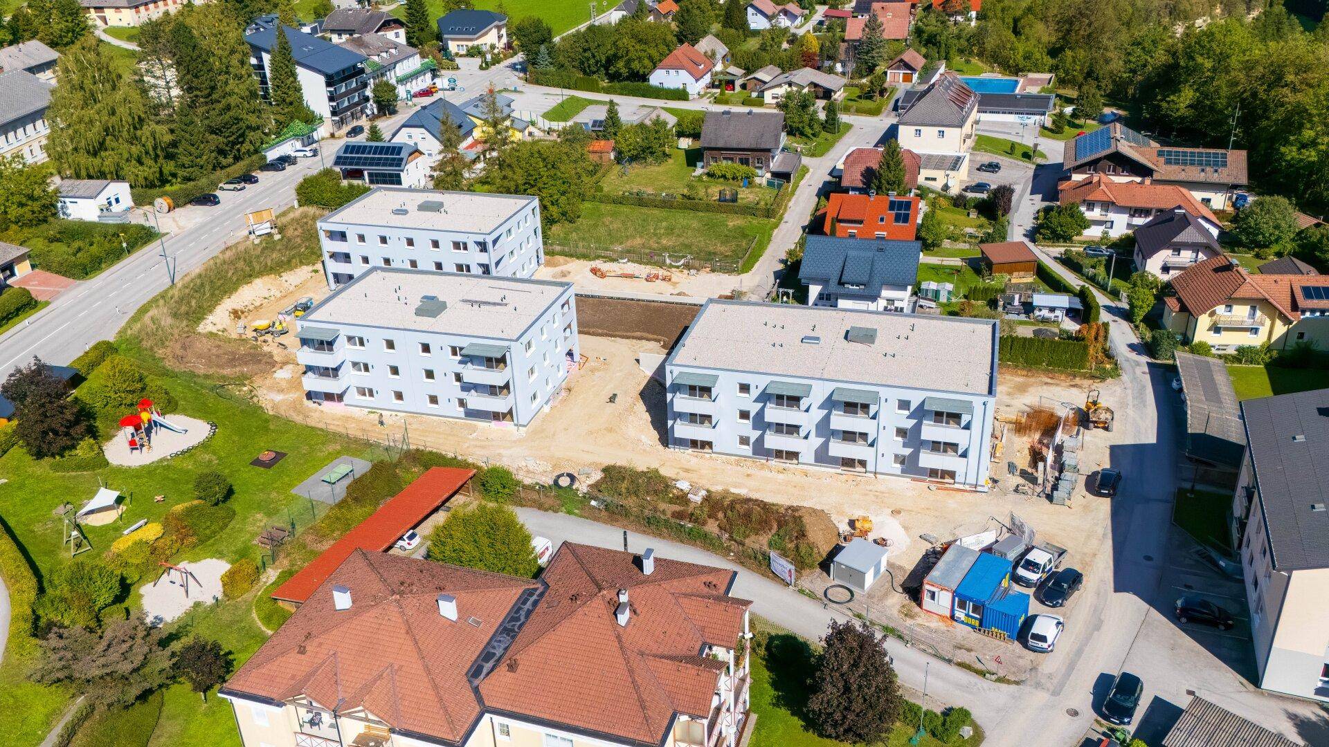 Luftaufnahme von mehreren neuen Wohngebäuden in einer grünen Wohngegend mit Bergblick und Spielplatz.