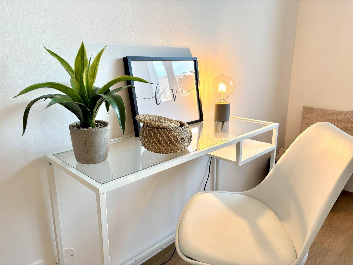 Heller Arbeitsbereich mit modernem Schreibtisch, Glasplatte und dekorativer Beleuchtung in einem Schlafzimmer.