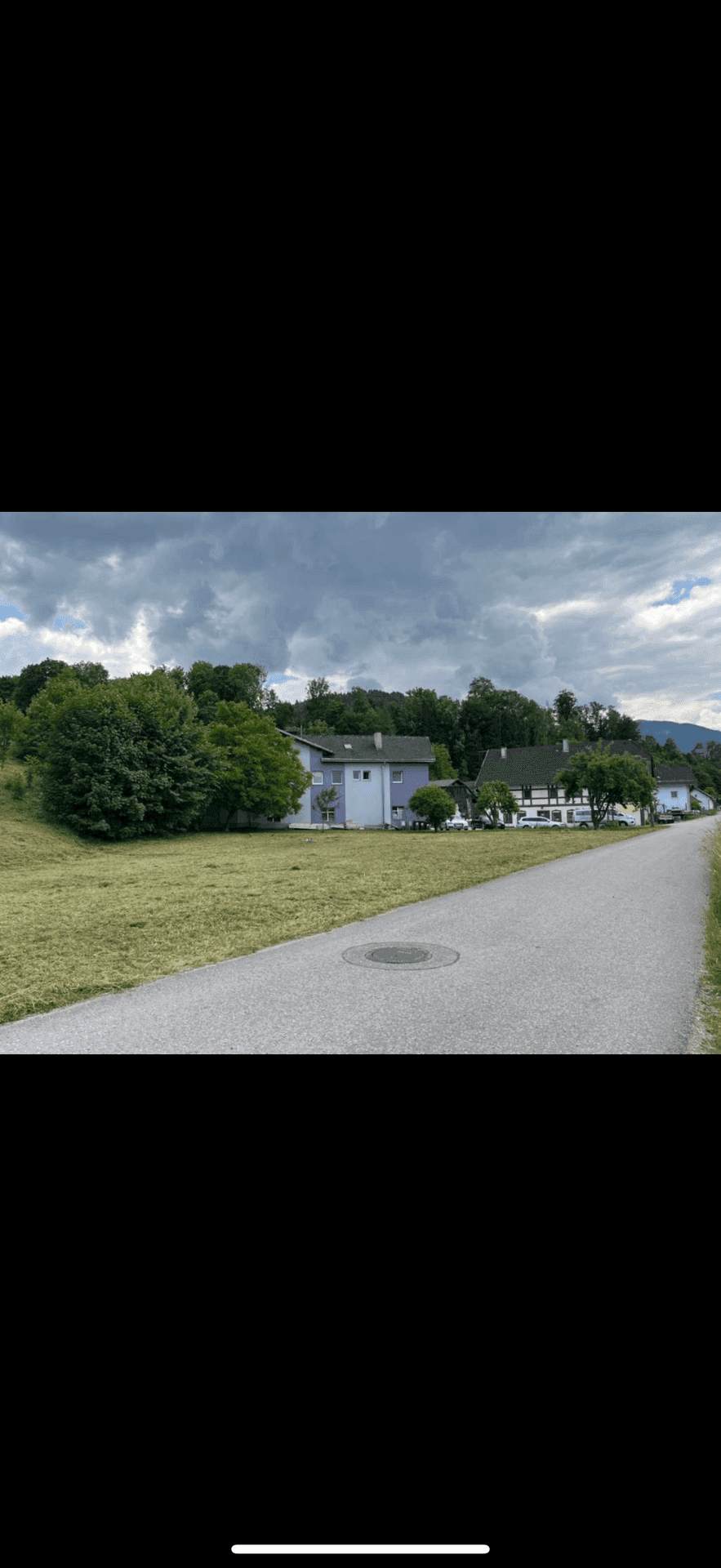 Straße entlang eines Hanggrundstücks mit Wohnhäusern und grüner Umgebung.