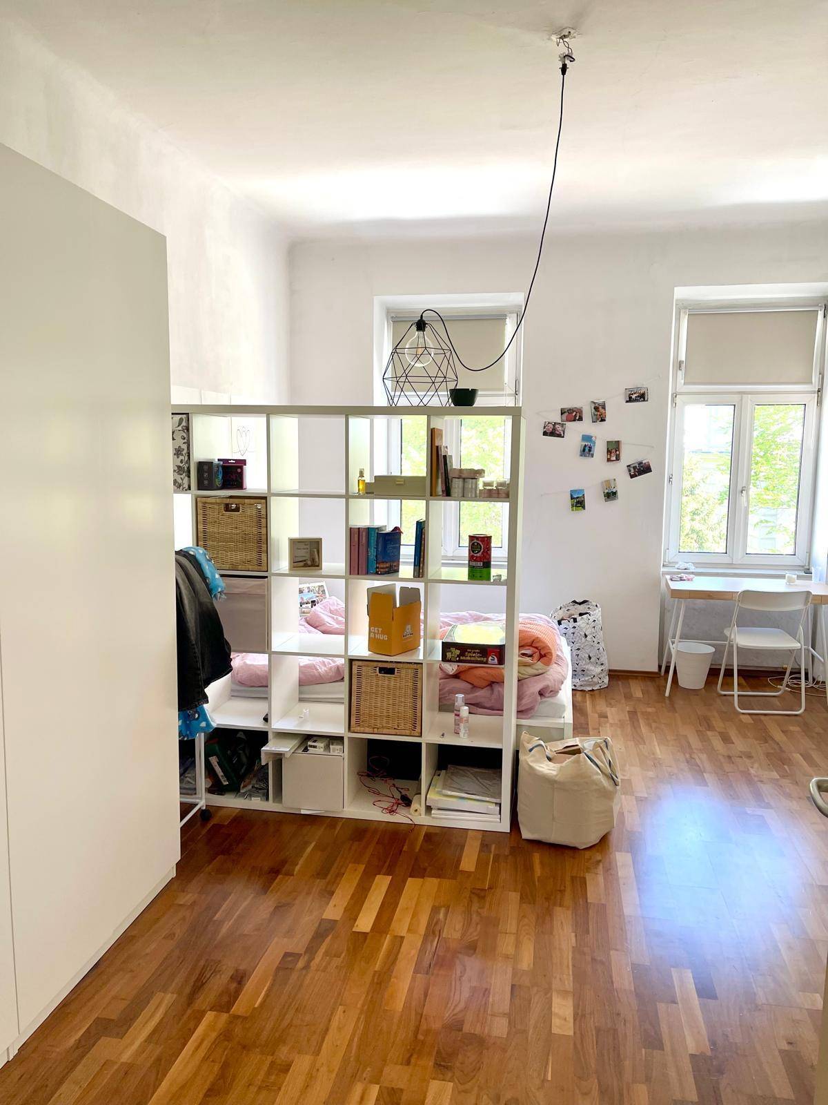 Geräumiges Schlafzimmer mit Holzboden, Raumteiler und viel Tageslicht durch die Fenster.
