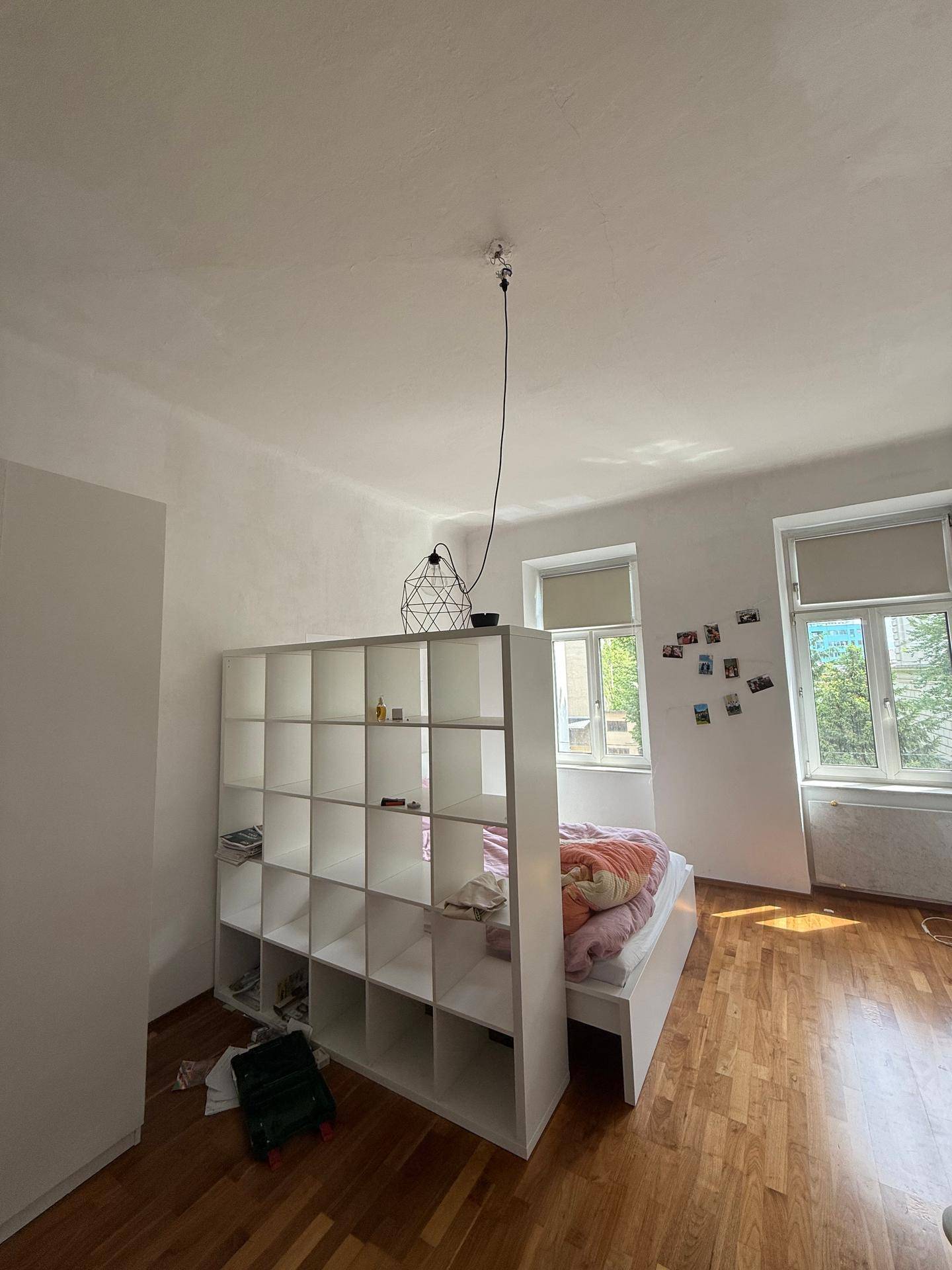 Heller Schlafbereich mit großem Fenster, Holzboden und einem praktischen Raumteiler-Regal.