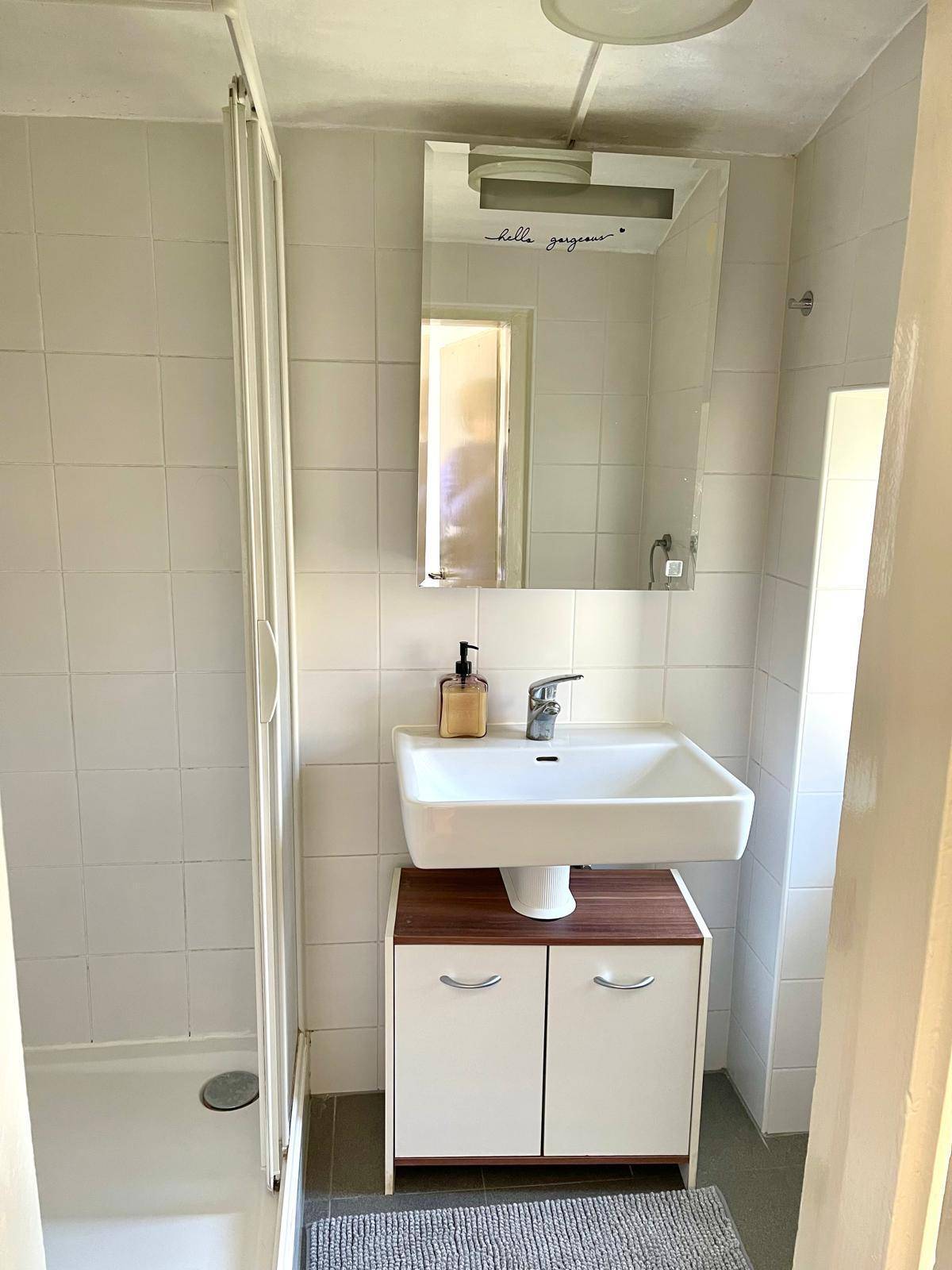 Funktionales Badezimmer mit Waschbecken, Spiegelschrank und praktischer Duschkabine.