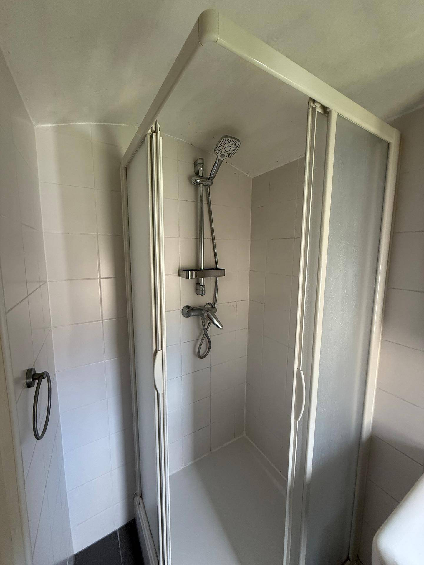 Funktionales Badezimmer mit Duschkabine, weißen Fliesen und einfacher, sauberer Ausstattung.