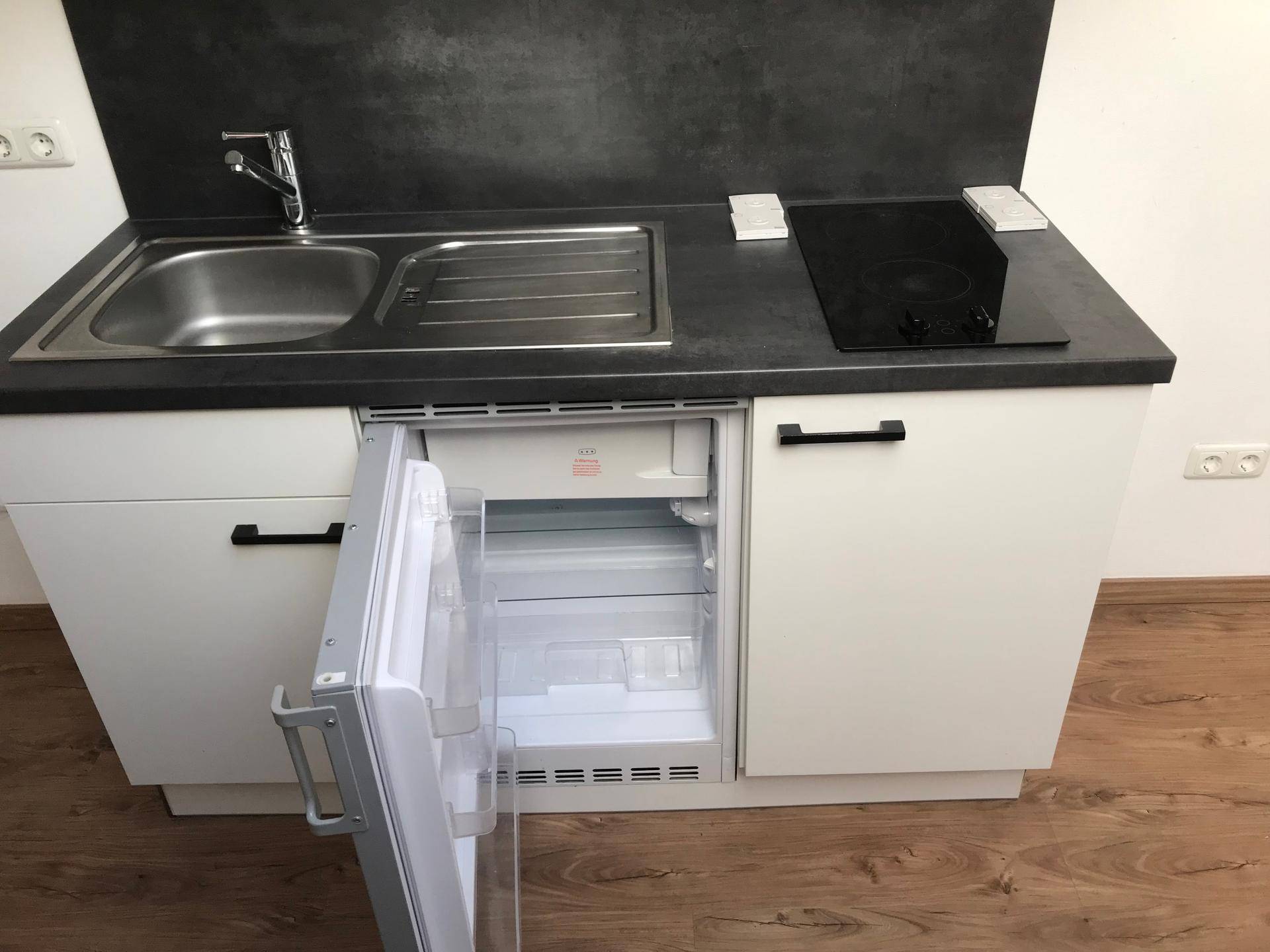 Detailansicht der Küchenzeile mit geöffnetem Kühlschrank und integriertem Kochfeld.