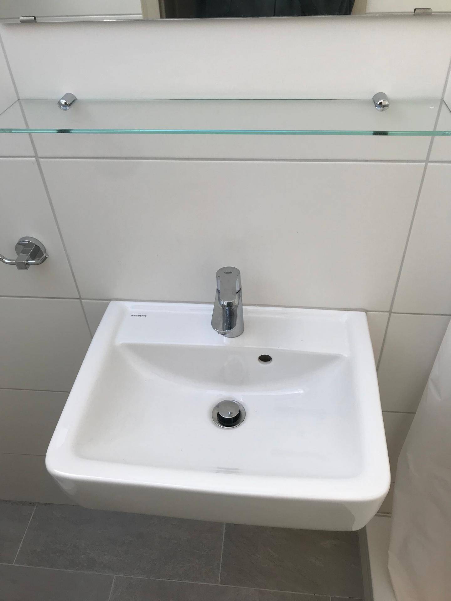 Modernes Waschbecken mit Chromarmatur und einer praktischen Glasablage über den Fliesen.