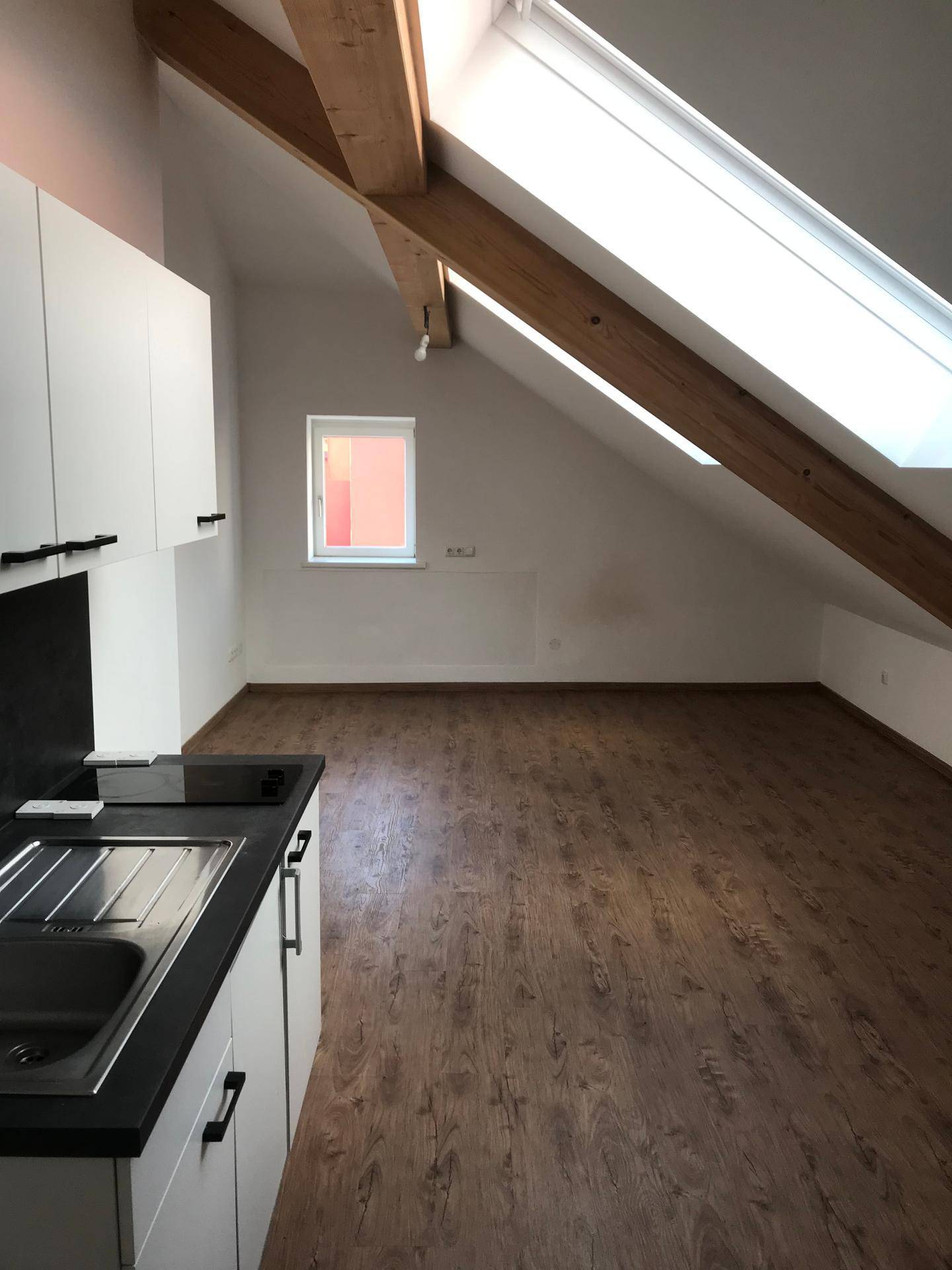Geräumiger Dachbodenraum mit Holzbalken, großem Dachfenster und einem kleinen Seitenfenster.