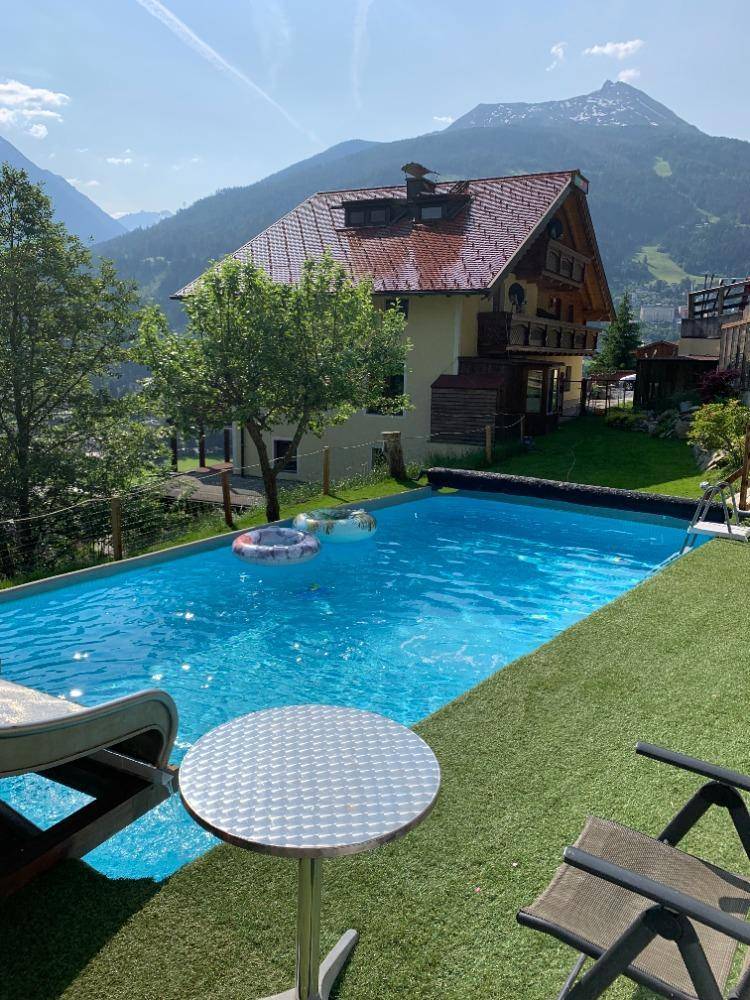Außenbereich mit großem Pool, Kunstrasen und Bergblick vor einem traditionellen Haus.