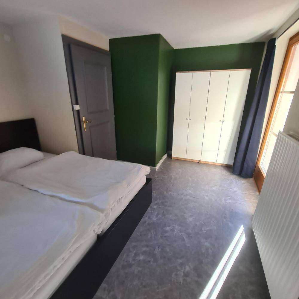 Schlafzimmer mit Doppelbett, grün gestrichener Wand und Zugang zu einem Balkon.
