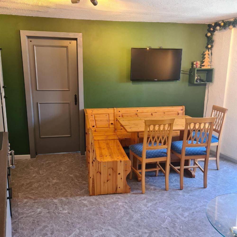 Gemütlicher Essbereich mit Eckbank aus Holz, Stühlen und grün gestrichener Wand.