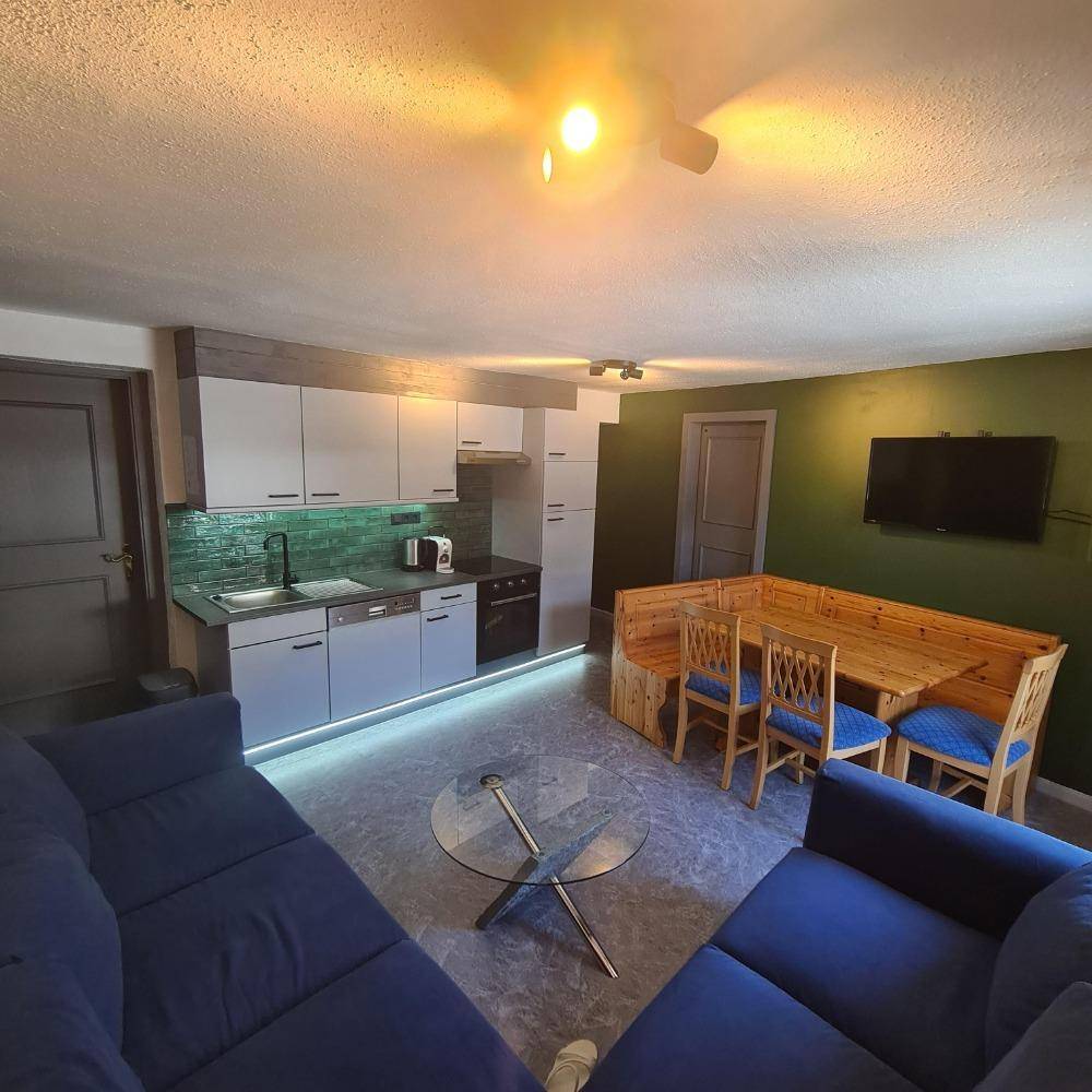 Offener Wohn- und Essbereich mit Küche, Holzeckbank und blauen Sofas.