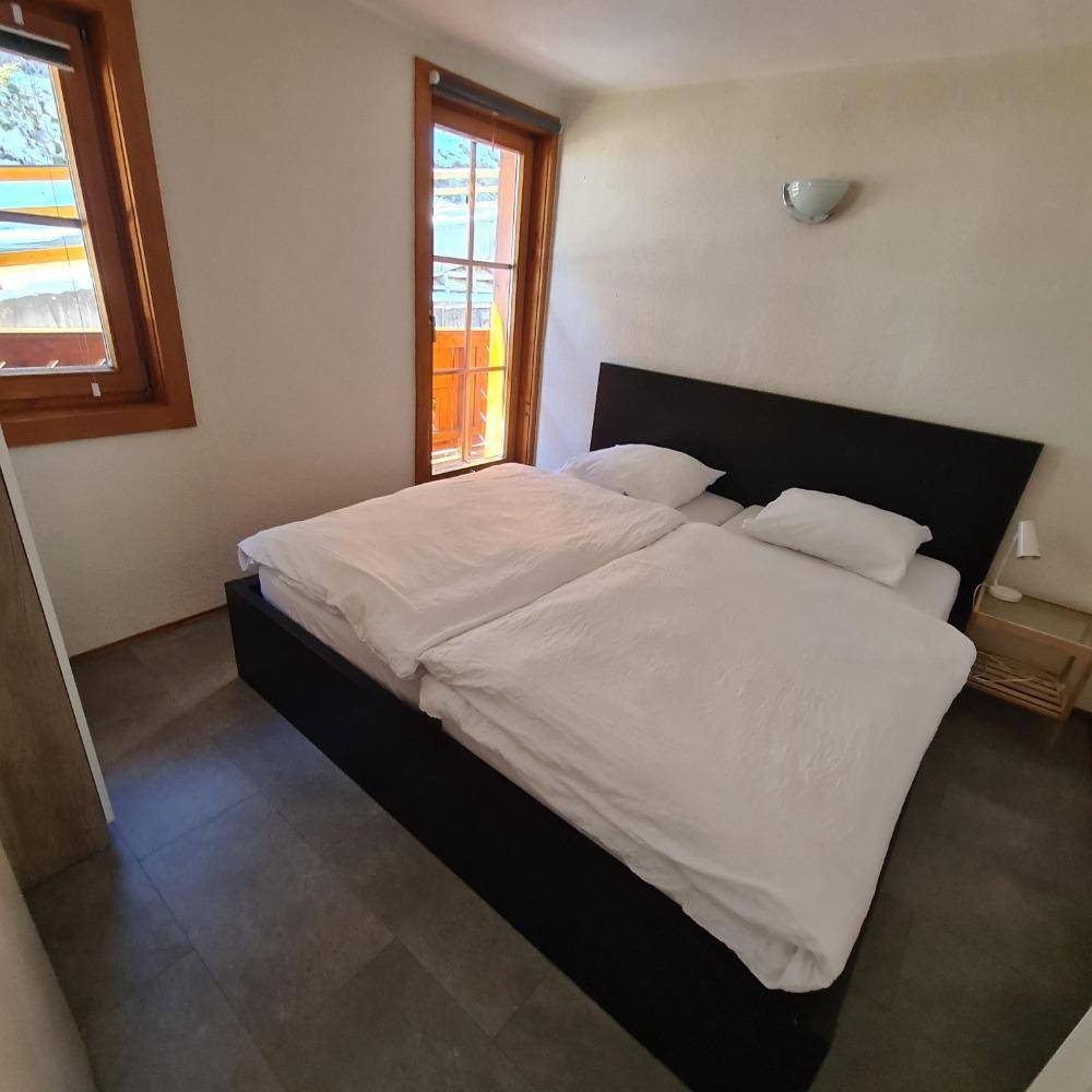 Helles Schlafzimmer mit Doppelbett, Holzbalkonfenstern und schlichtem Design.
