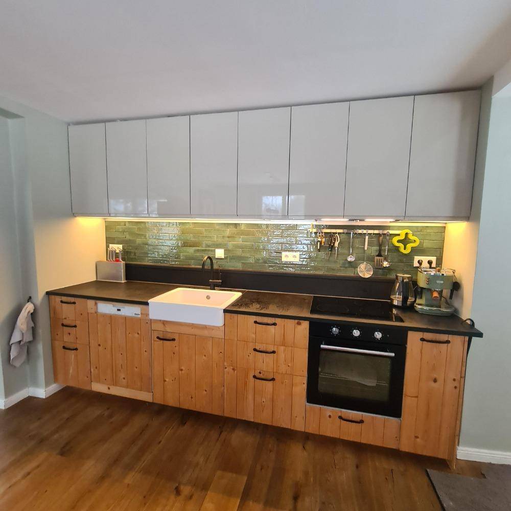 Moderne Küche mit Holzfronten, weißer Spüle und grünen Fliesen als Spritzschutz.