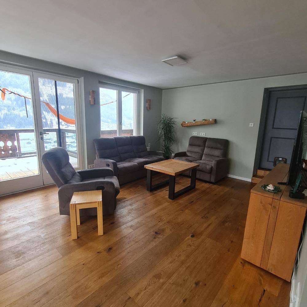 Helles Wohnzimmer mit Holzboden, bequemen Sofas und Zugang zu einem Balkon.