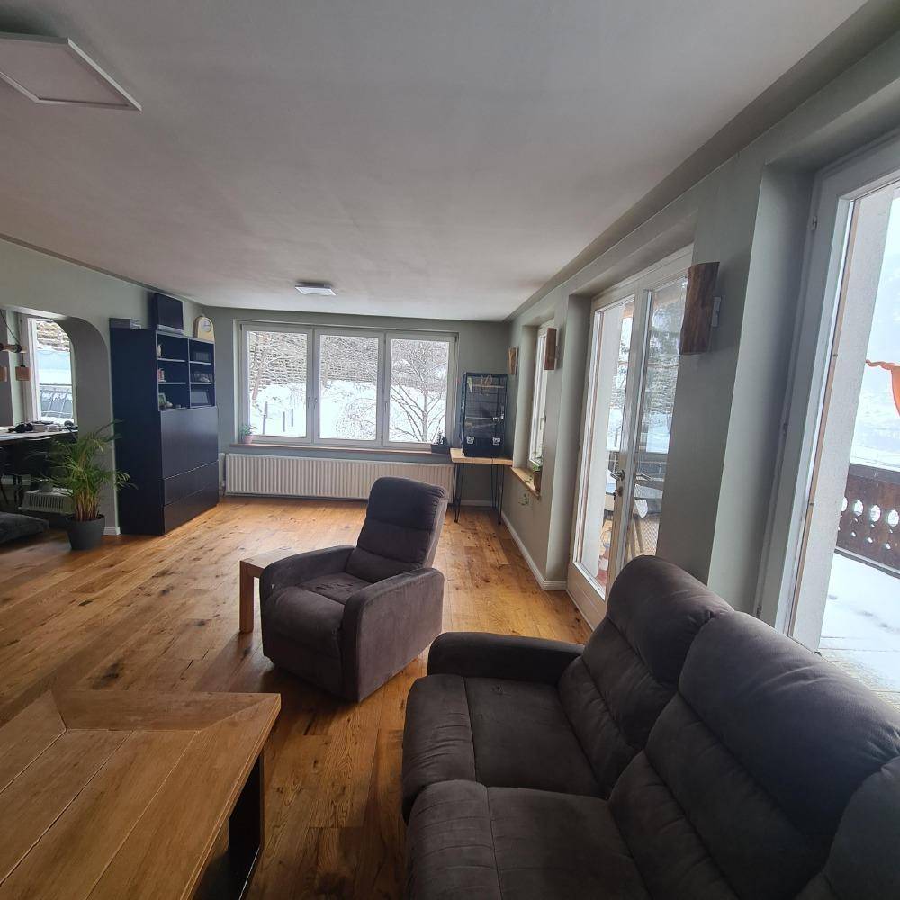Geräumiges Wohnzimmer mit Holzboden, großen Fenstern und Blick auf die verschneite Landschaft.