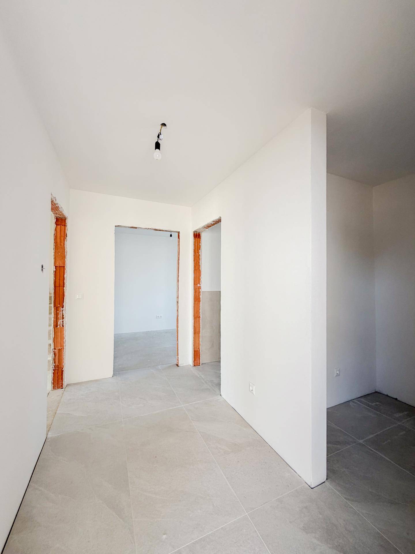 Eingangsbereich im Rohbau mit Fliesenboden und offenen Durchgängen zu weiteren Räumen.