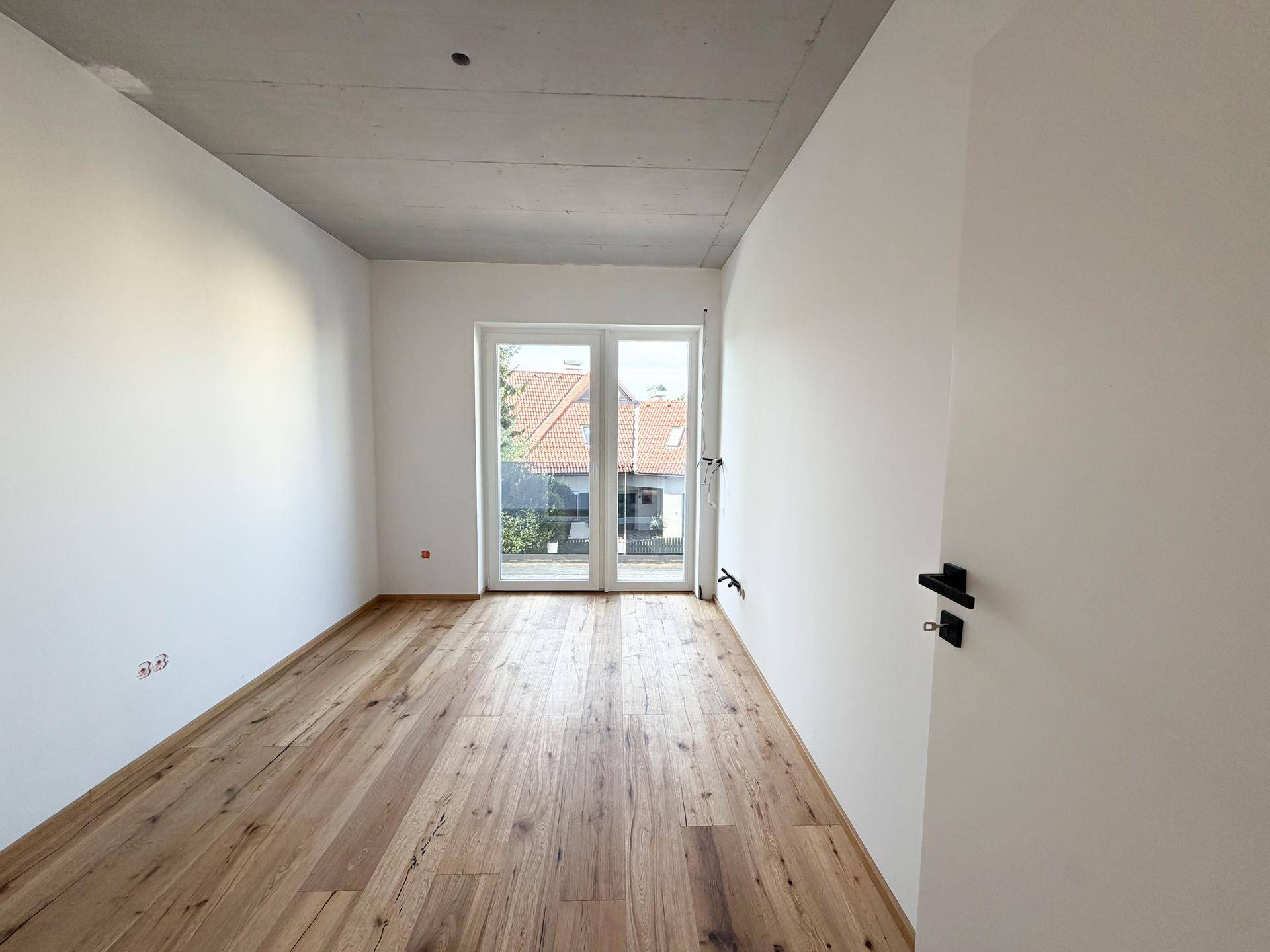 Schlafzimmer mit Holzboden, weiß gestrichenen Wänden und Balkonzugang.