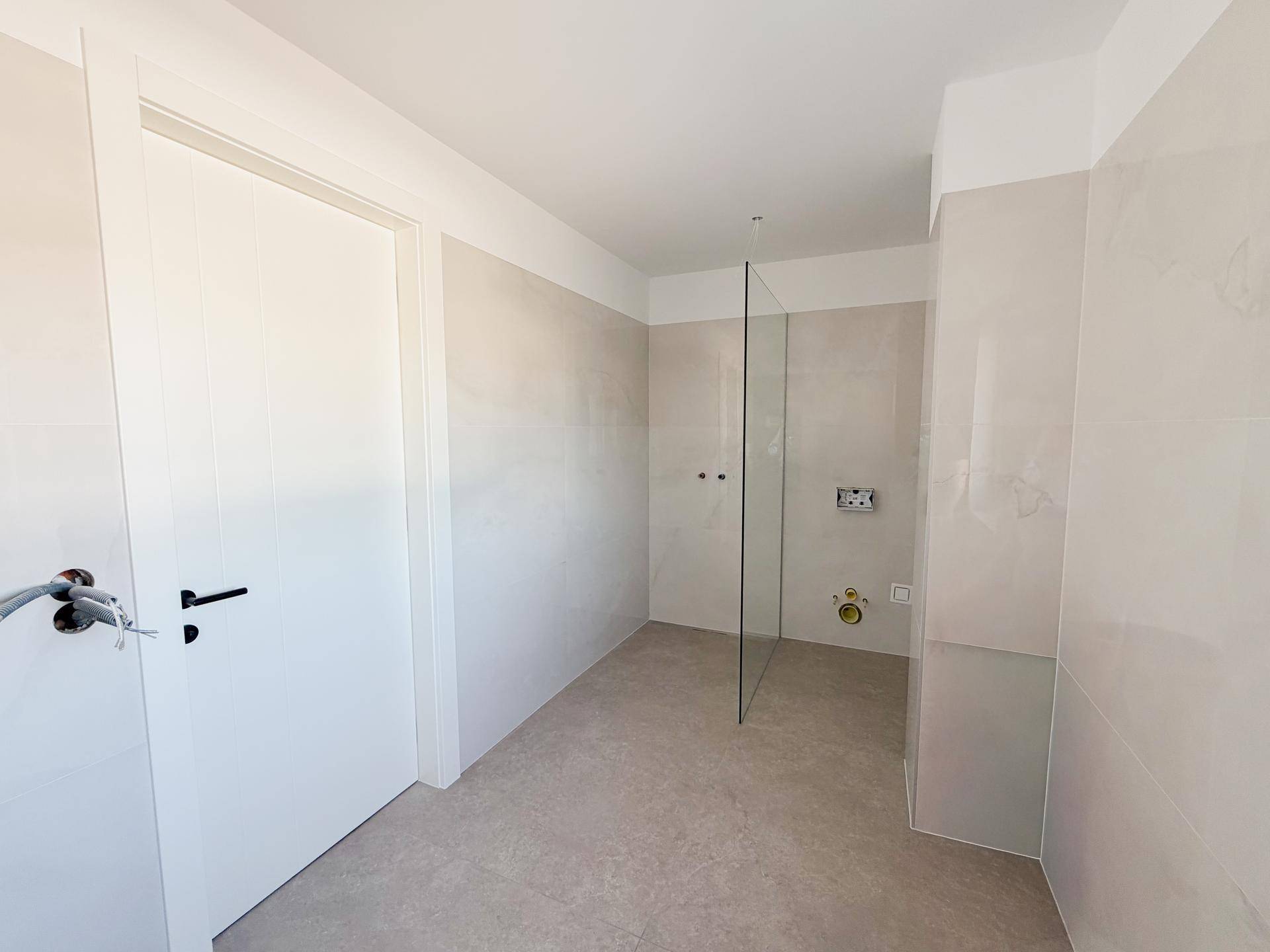 Modernes Badezimmer im Rohbau mit hellen Fliesen und vorbereiteter Duschkabine.