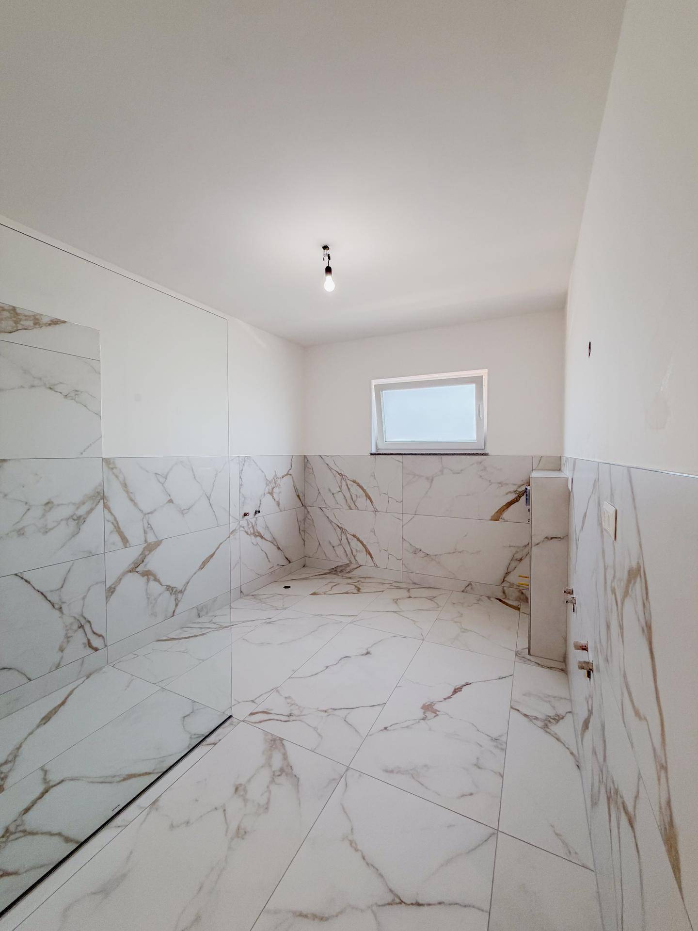 Modernes Badezimmer im Rohbau mit eleganten Marmorfliesen und Fenster für Tageslicht.