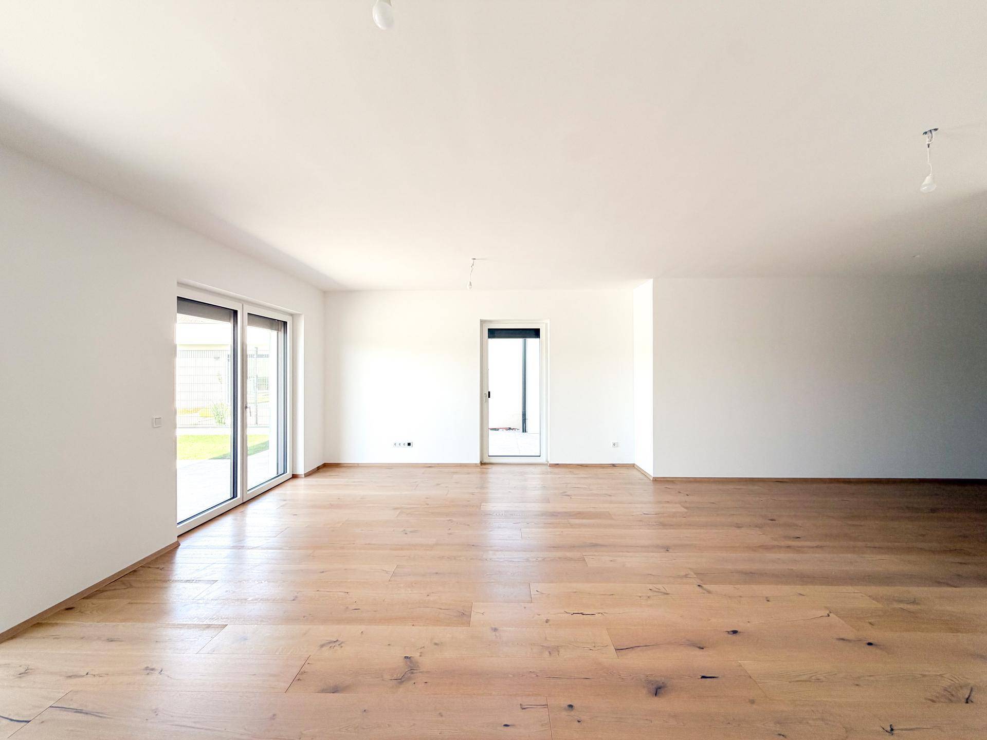 Lichtdurchfluteter Wohnbereich mit Holzboden und Zugang zum Garten durch große Fenster.