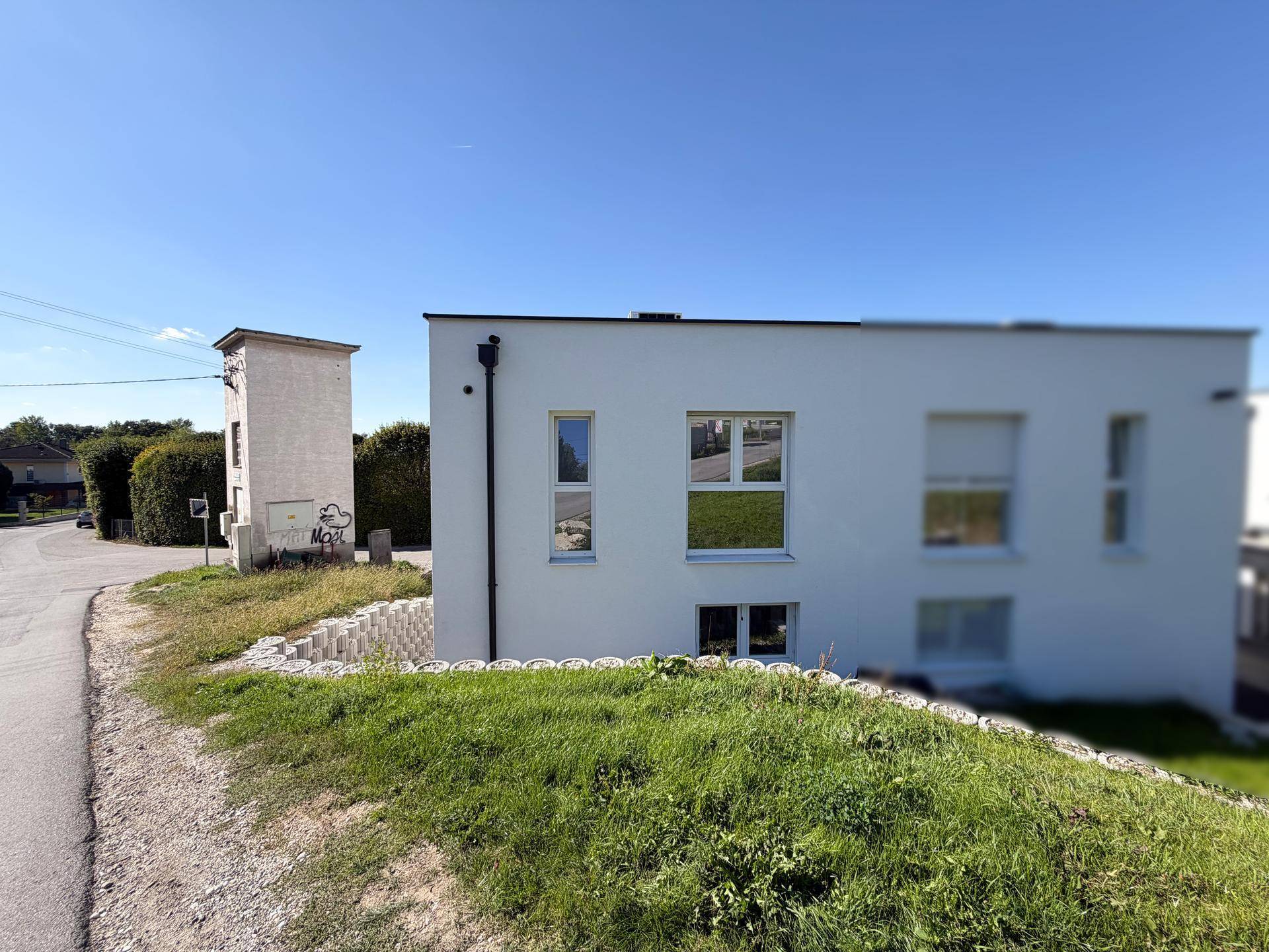 Seitenansicht des modernen Gebäudes mit weißer Fassade und umliegender Landschaft.