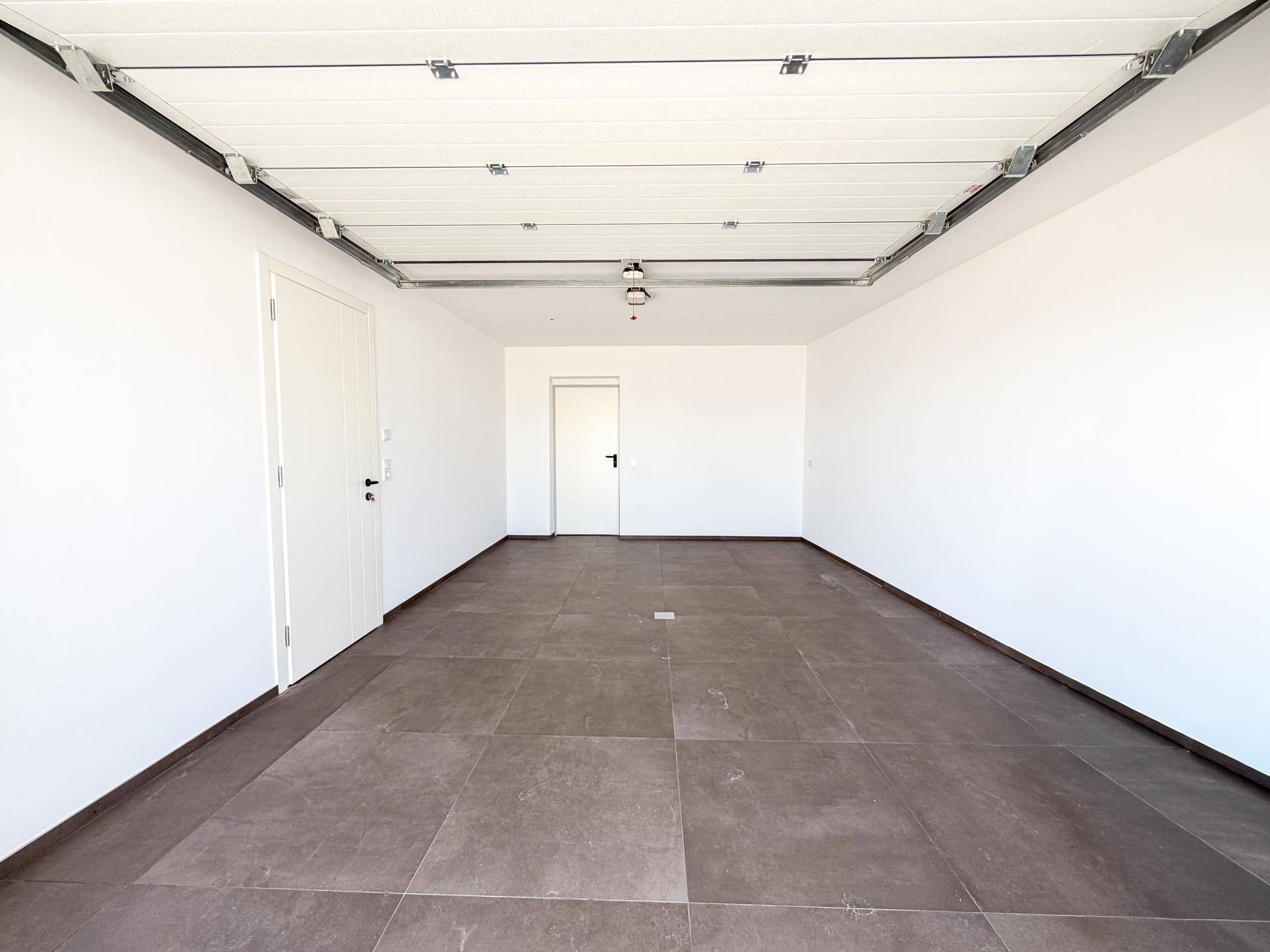 Geräumige Garage mit Fliesenboden und automatischem Garagentor-Mechanismus.