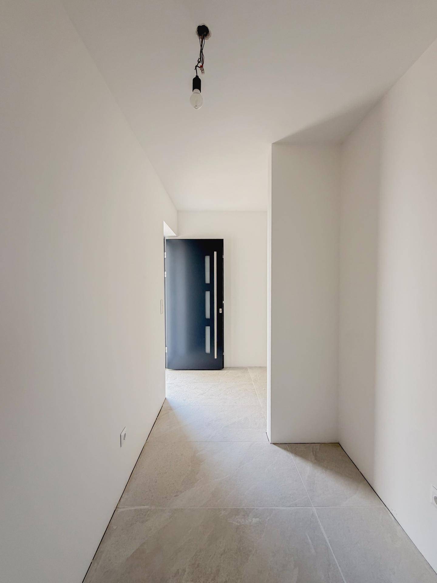 Langer, heller Flur im Rohbau mit Betonboden und Blick zur Eingangstür.