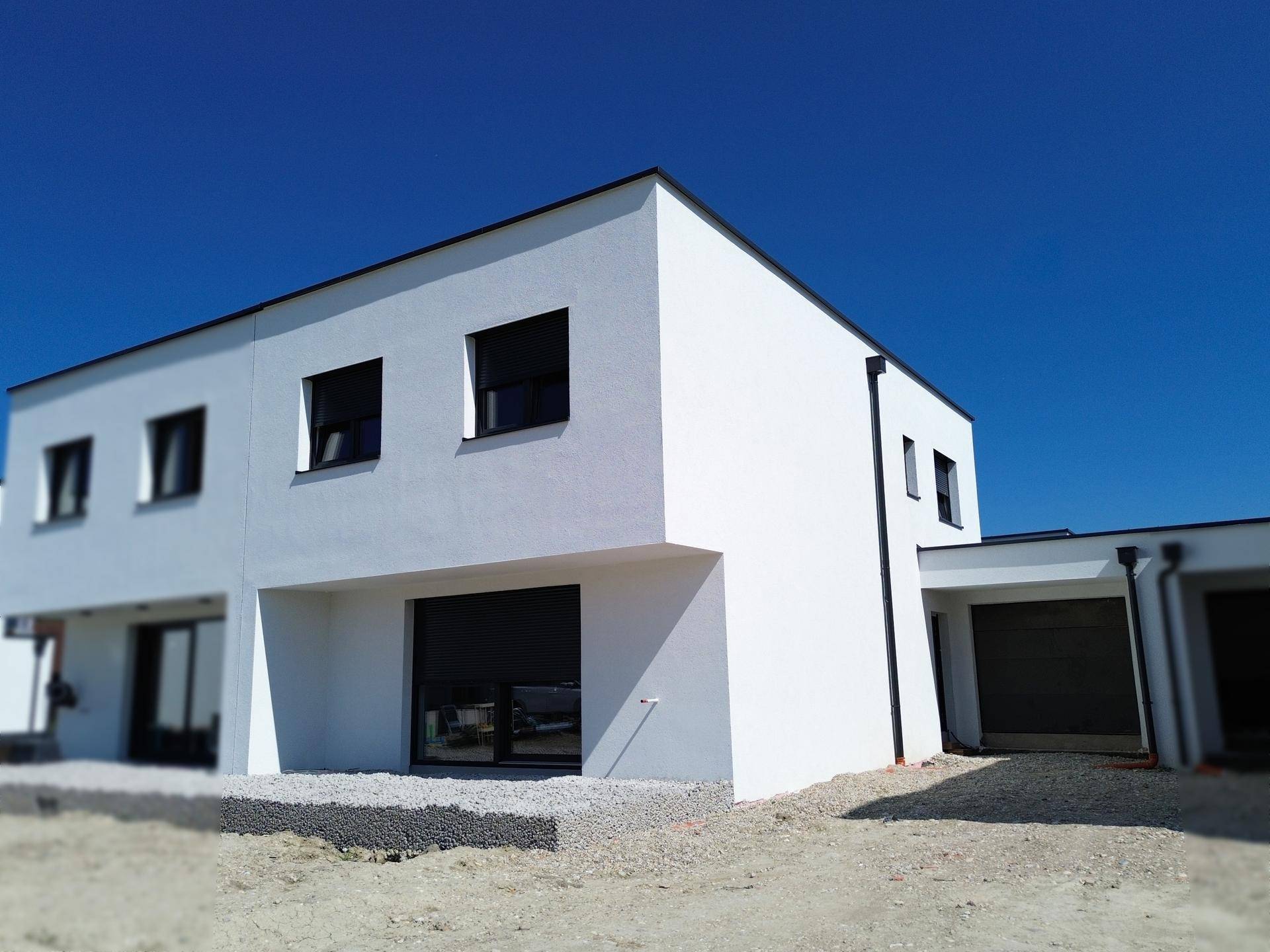 Nahaufnahme eines modernen Neubaus mit weißer Fassade, schwarzen Fenstern und geschlossenen Rollläden.
