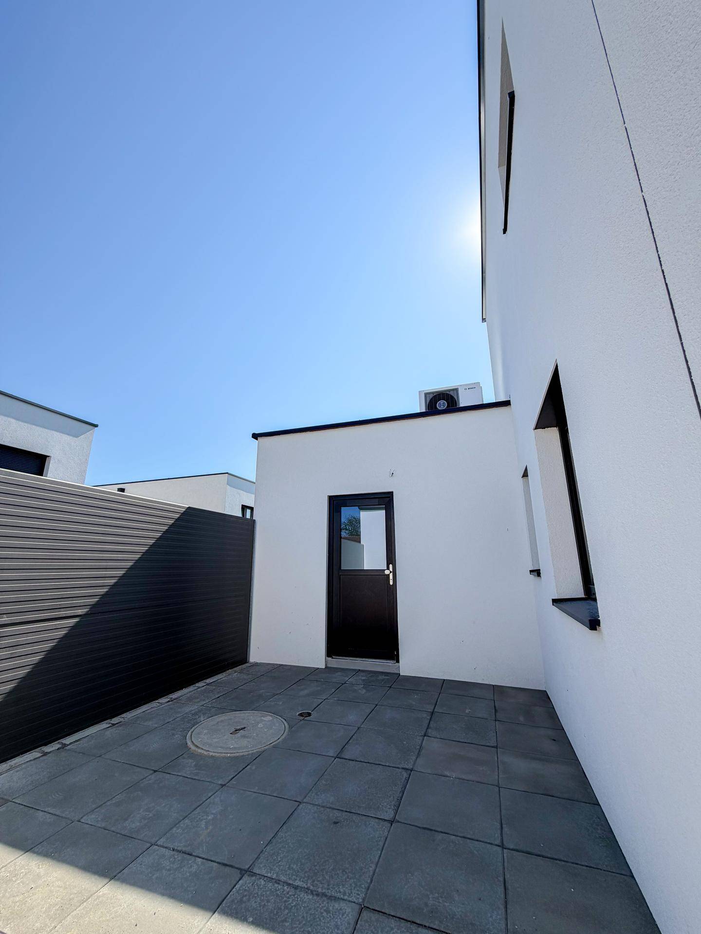 Kleiner gepflasterter Außenbereich mit Türzugang und Klimaanlage an der Wand.