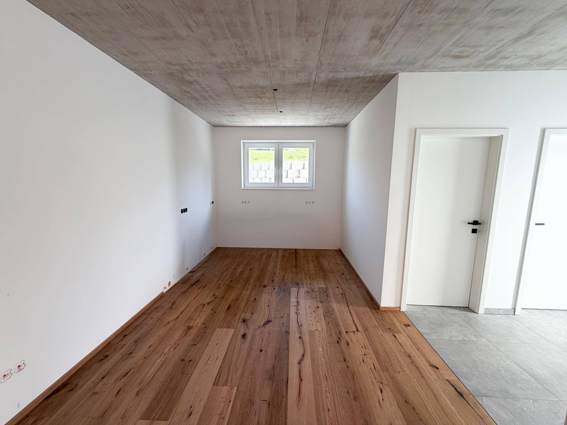 Leeres Zimmer mit Holzboden, weiß gestrichenen Wänden und einem Fenster.