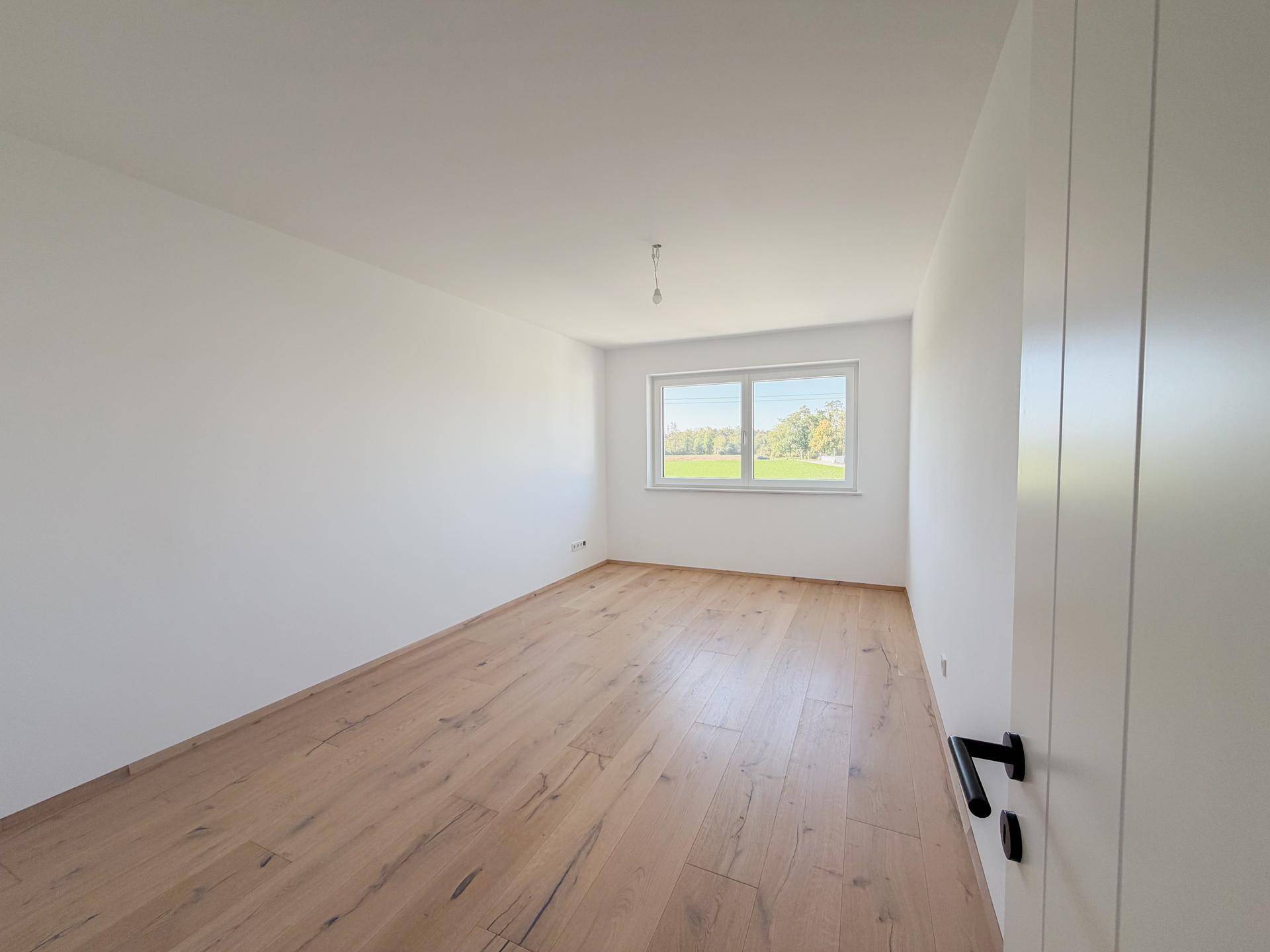Geräumiges Schlafzimmer mit Eichenparkettboden und Blick ins Grüne durch das Fenster.