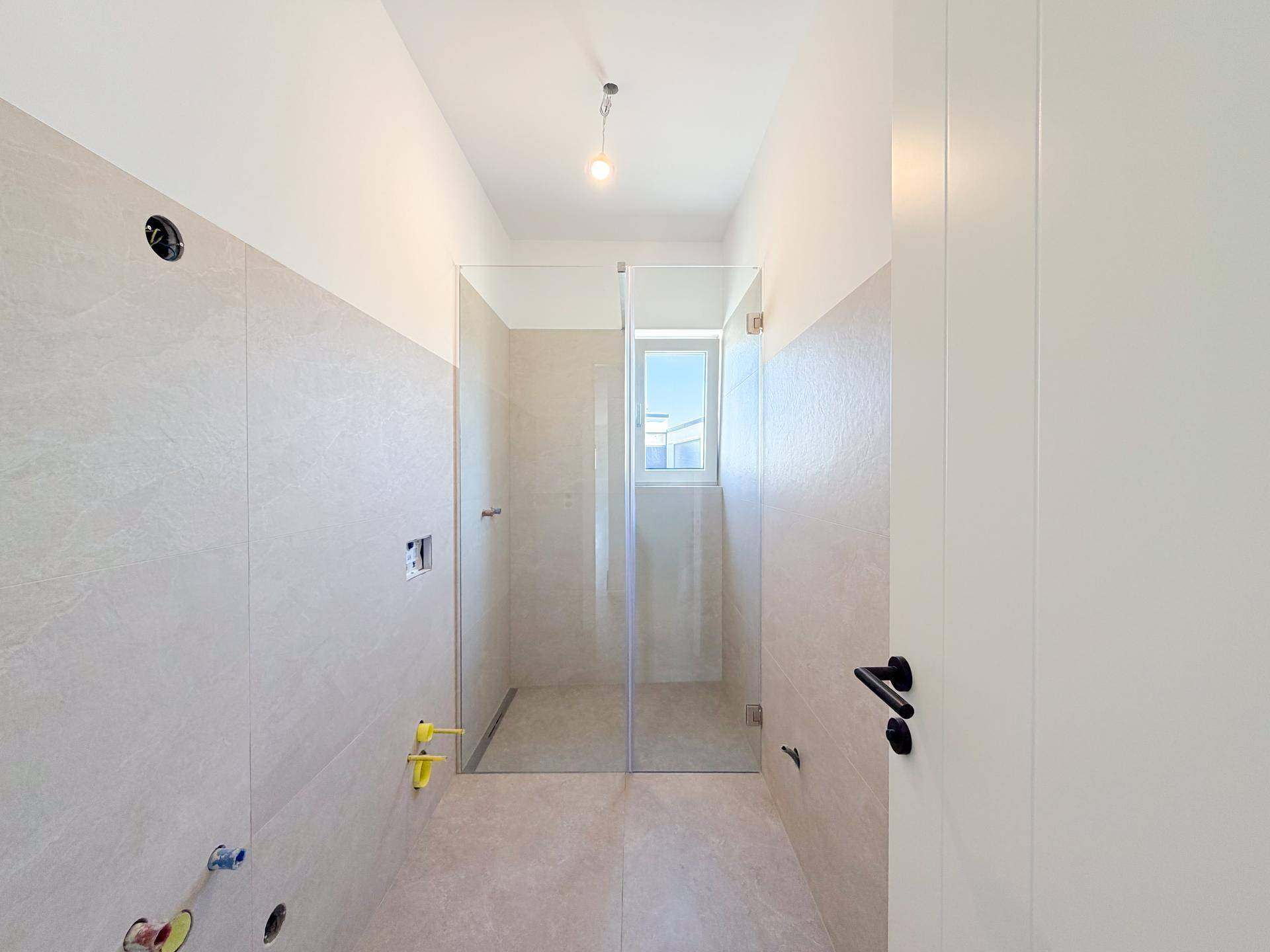 Modernes Badezimmer im Rohbau mit hellen Fliesen und vorbereiteter Duschkabine.