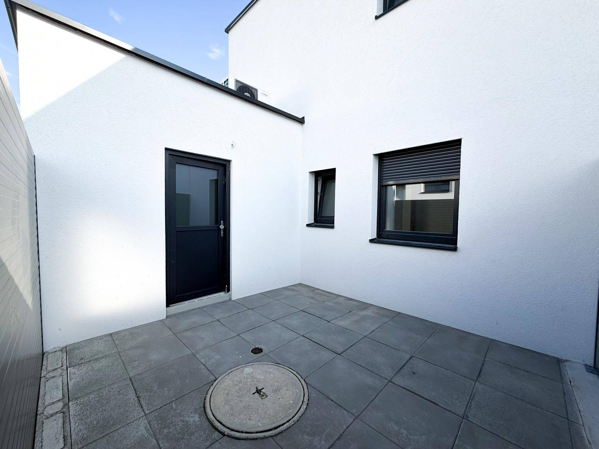 Kleiner gepflasterter Patio-Bereich mit Sichtschutz und Zugang zum Haus.