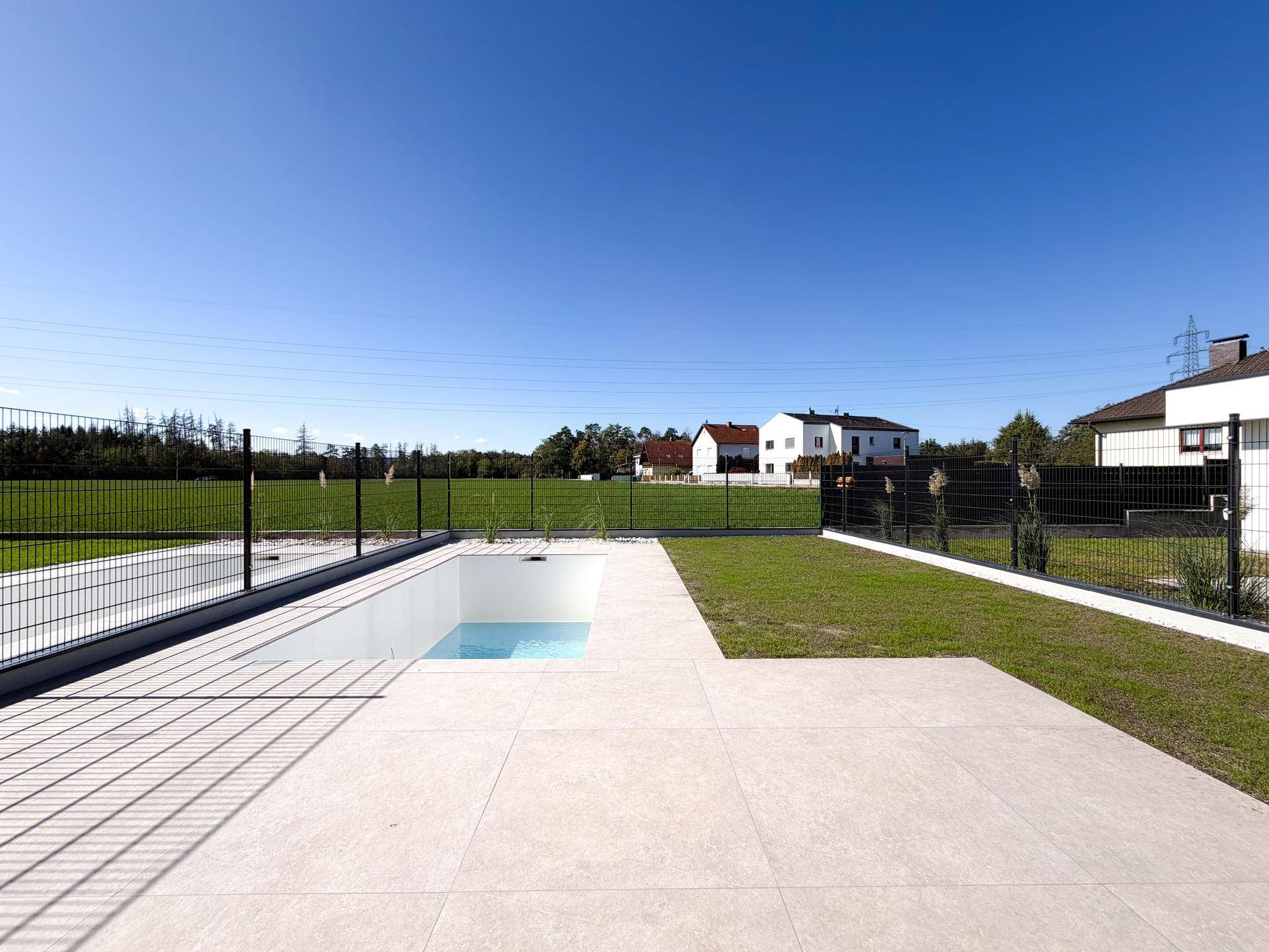 Moderner Poolbereich mit gepflasterter Terrasse und Blick auf die umliegende Natur.