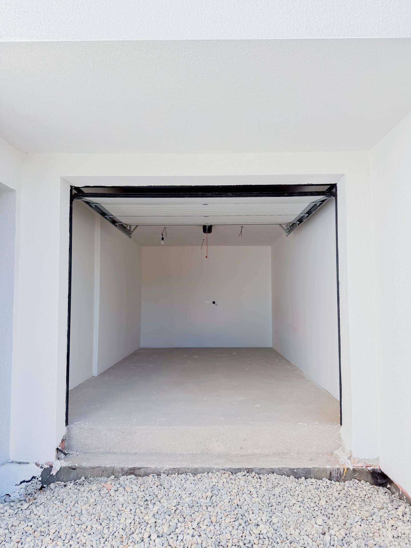 Leere Garage im Rohbau mit Betonboden und offenem Garagentor.