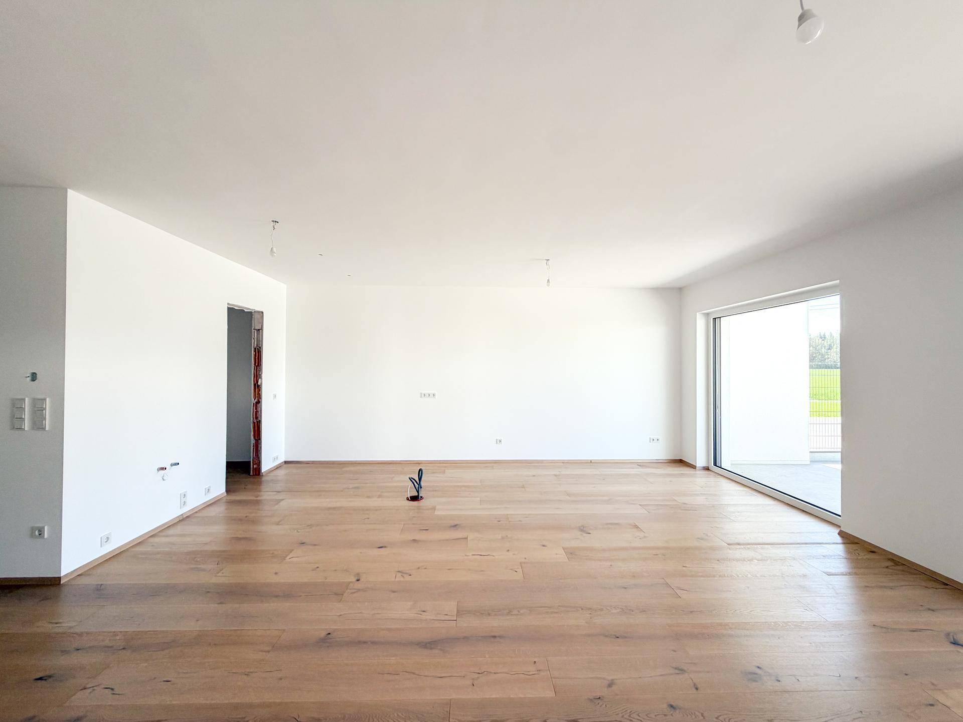 Offener Wohnraum mit Eichenparkettboden und weitem Blick durch das große Fenster.
