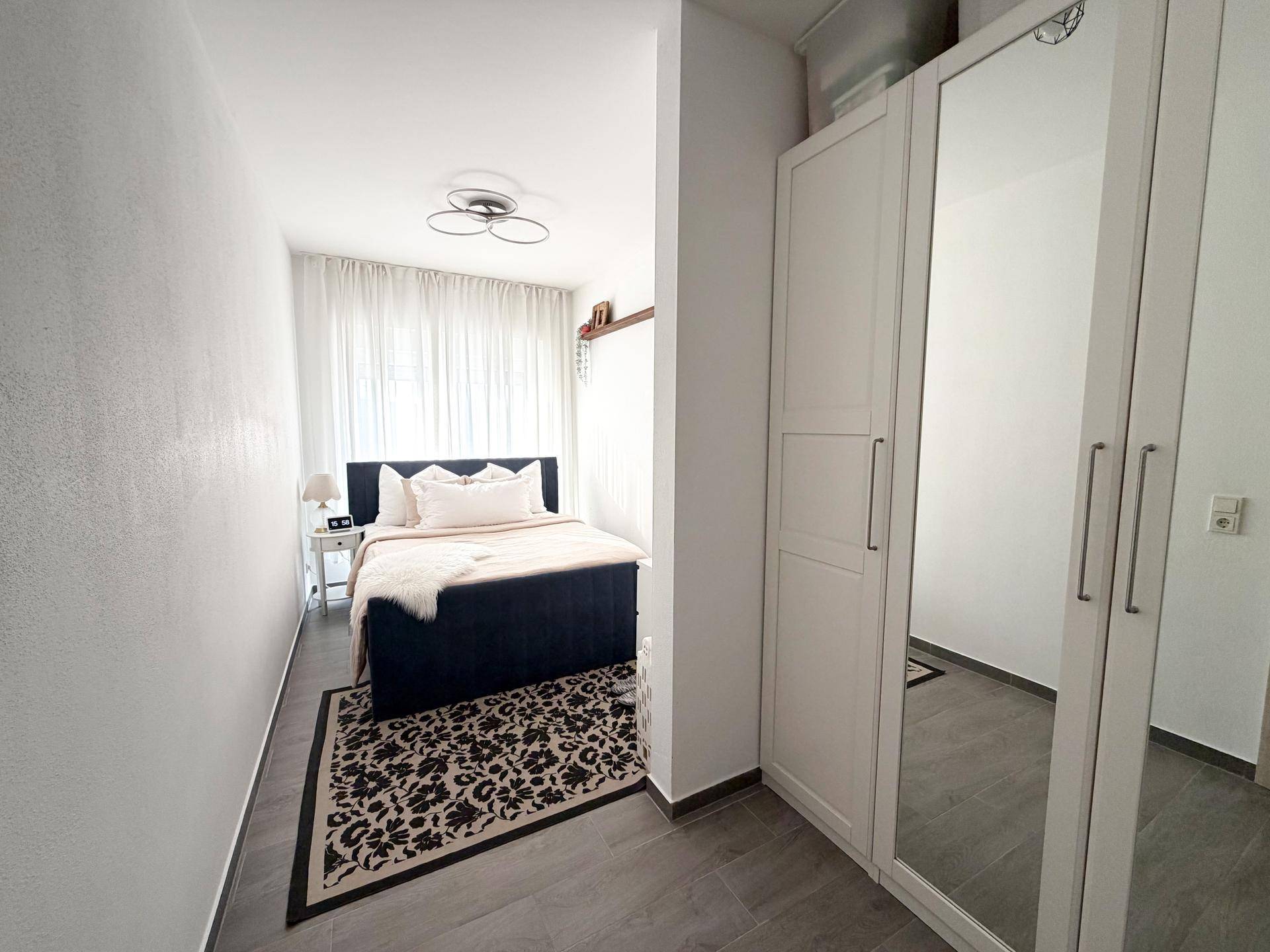 Helles Schlafzimmer mit Doppelbett, Spiegelschrank und Teppichboden.