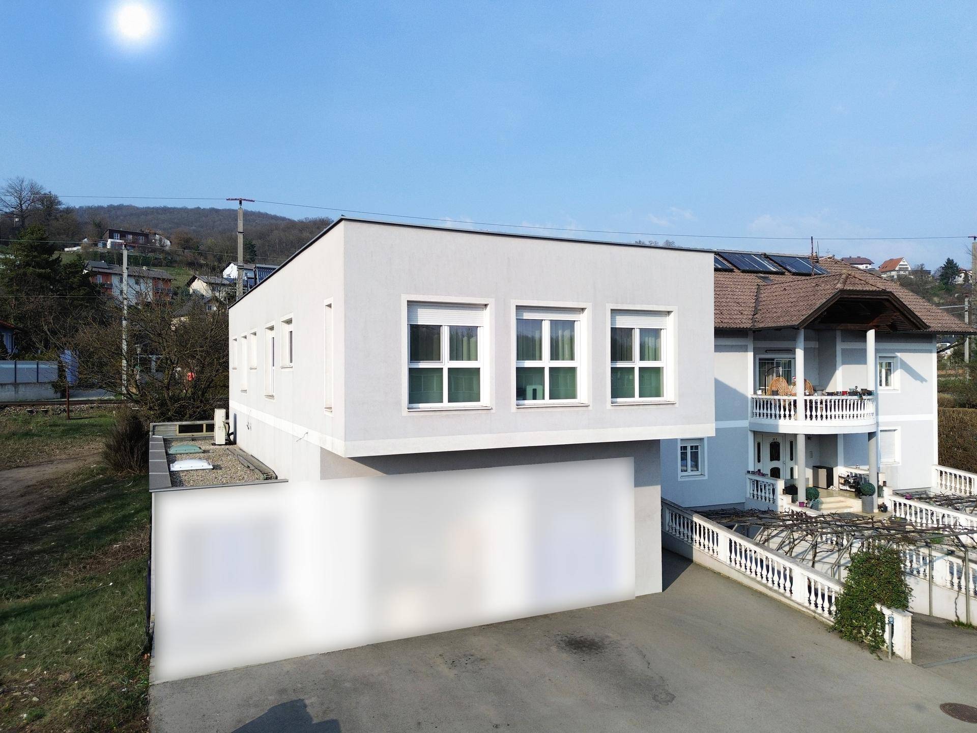 Modernes Gebäude mit weißer Fassade und Flachdach in sonniger Umgebung.