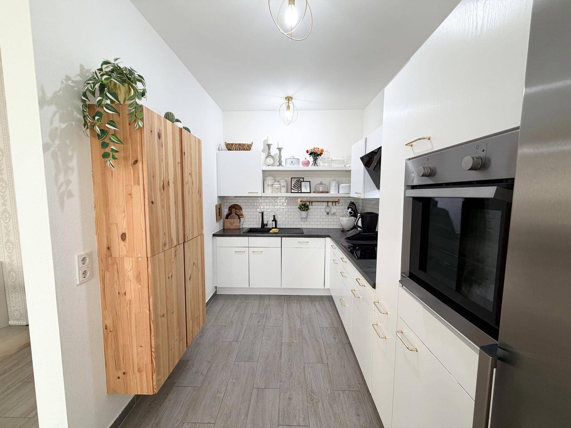 Schmale, moderne Küche mit weißen Schränken, Holzelementen und integriertem Backofen.