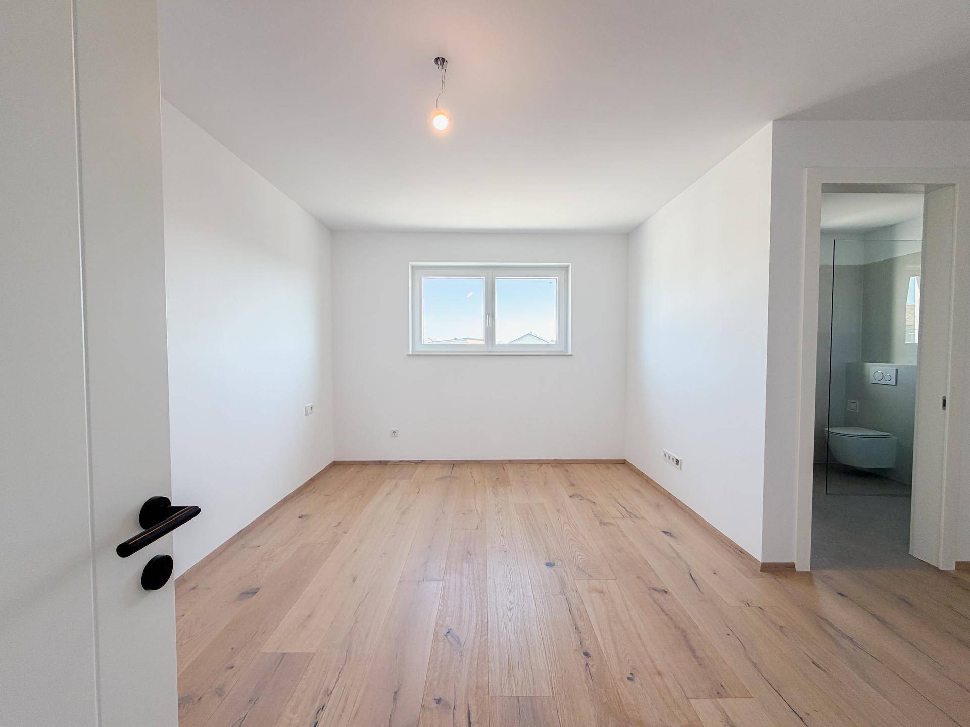 Helles Schlafzimmer mit Eichenparkettboden und direktem Zugang zum modernen Badezimmer.