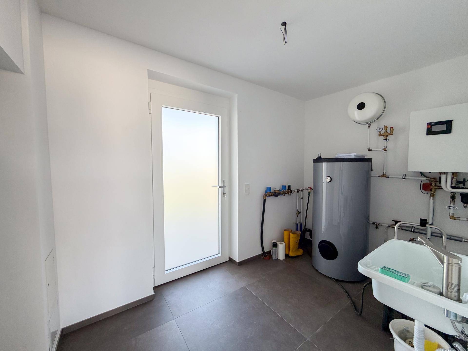 Praktischer Hauswirtschaftsraum mit Warmwasserspeicher, Waschbecken und Fliesenboden.
